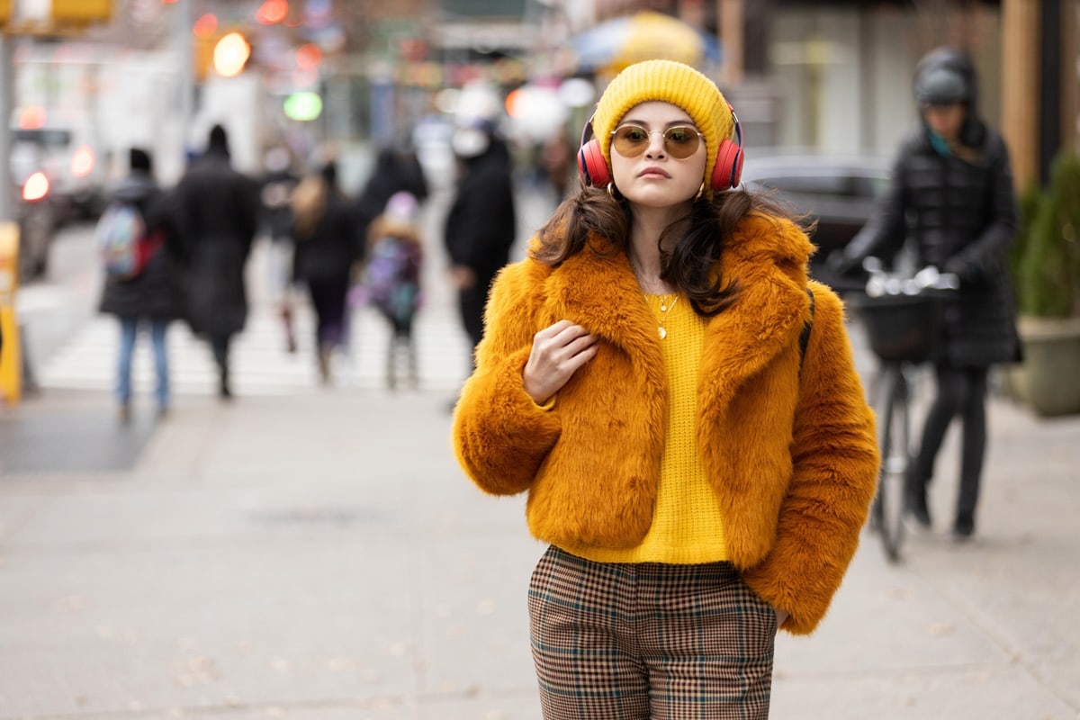 Selena Gomez wears a Michael Kors cropped fur jacket with a mustard jacket, a matching knit beanie, and plaid pants as Mabel Mora in the American mystery comedy-drama television series Only Murders in the Building