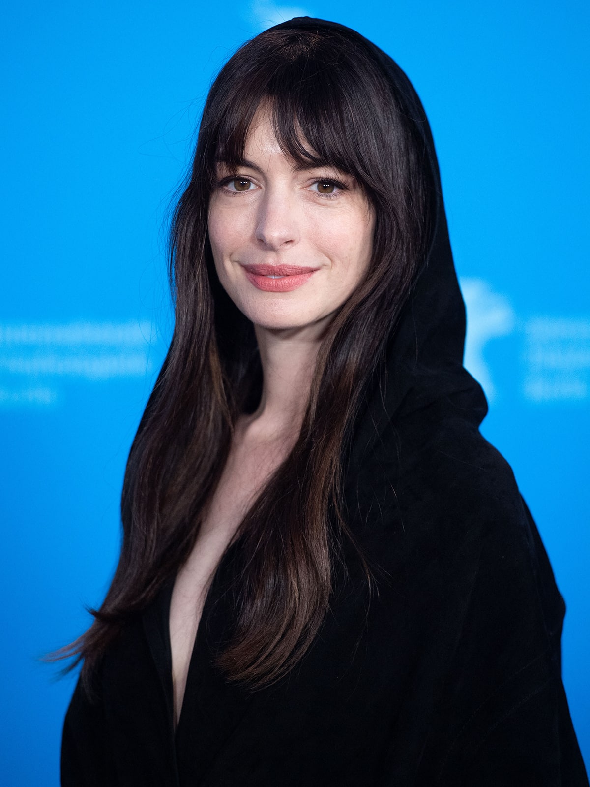 Anne Hathaway styles her dark tresses in waves and wears a natural makeup-look with a bright matte lip color