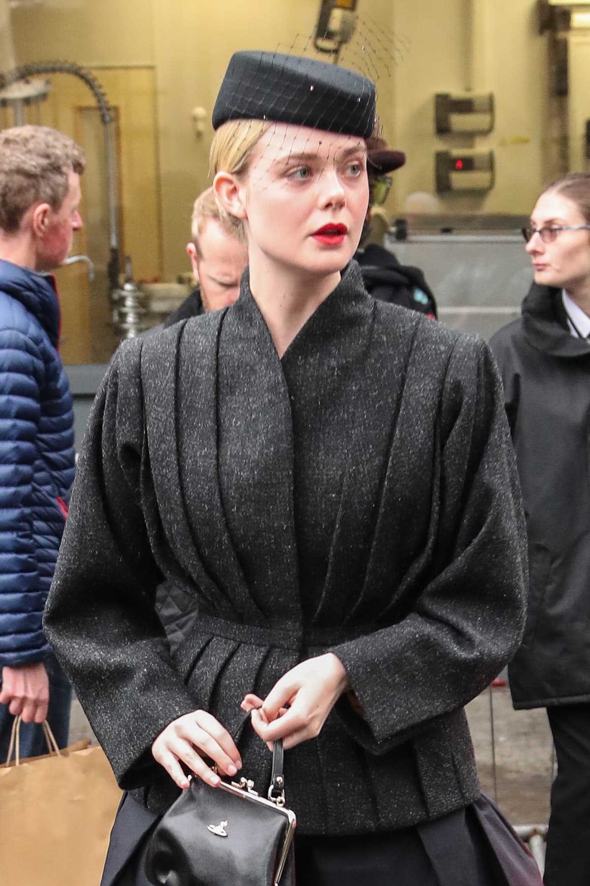 Elle Fanning adds a pop of red lipstick to her outfit and accessorizes with a veiled black pillbox hat and a Vivienne Westwood top-handle purse