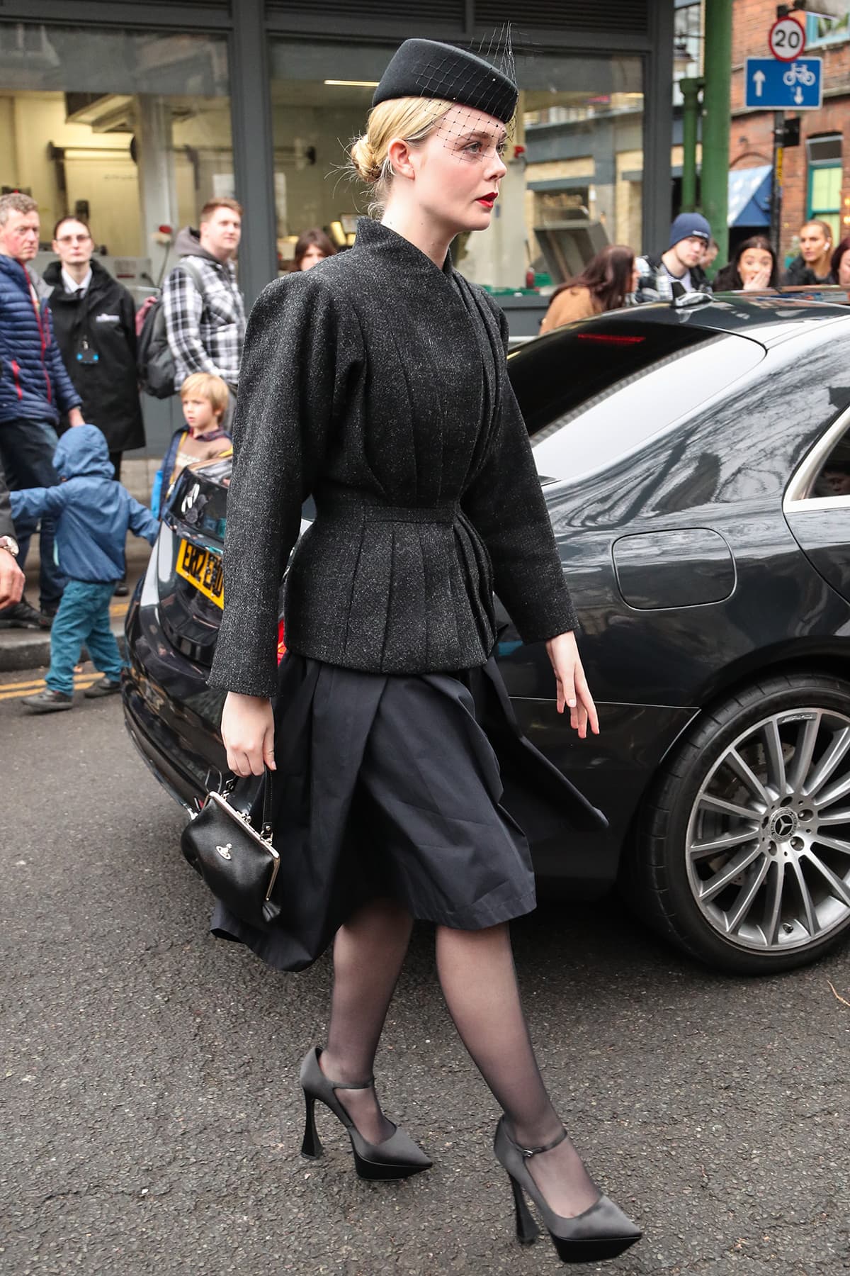 Elle Fanning attends Vivienne Westwood's memorial service in a black knee-length dress with a pleated wool jacket and high-heel Mary Jane pumps