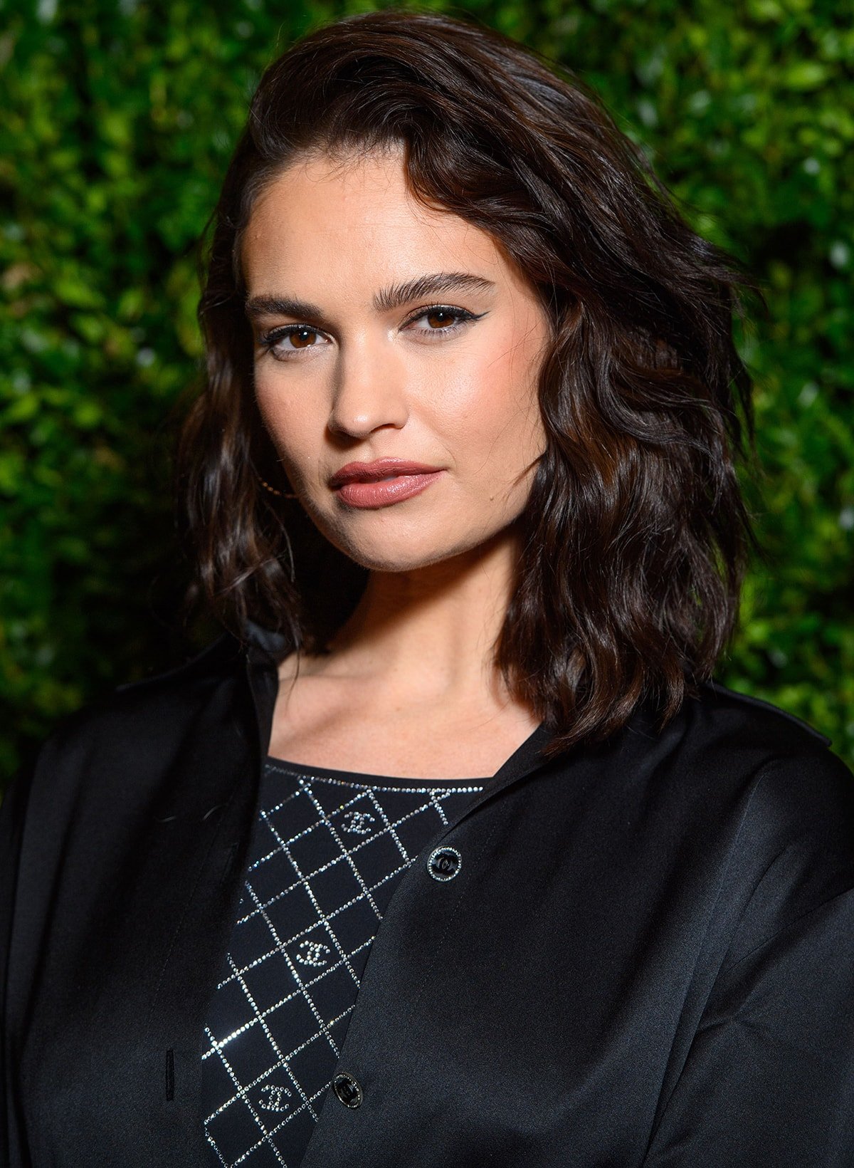 Lily James wears her tresses in side-swept retro curls and defines her features with winged eyeliner, rosy blush, and matching lip color