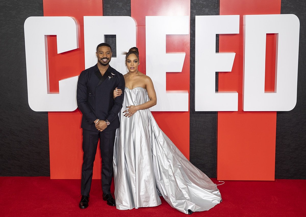 On-screen couple Michael B. Jordan and Tessa Thompson pose arm-in-arm, with Michael in a Prada black suit and Tessa in a reflective Robert Wun gown