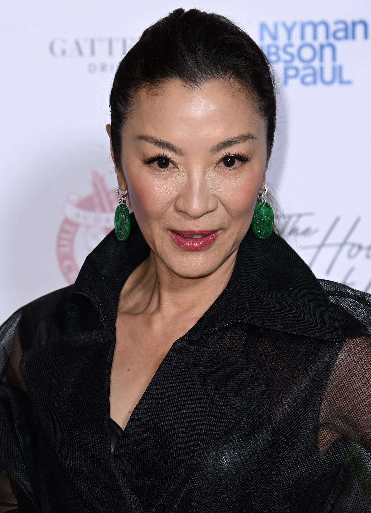 Michelle Yeoh pulls her hair into a ponytail and adds a pop of color to her black ensemble by accessorizing with emerald green sculptural earrings