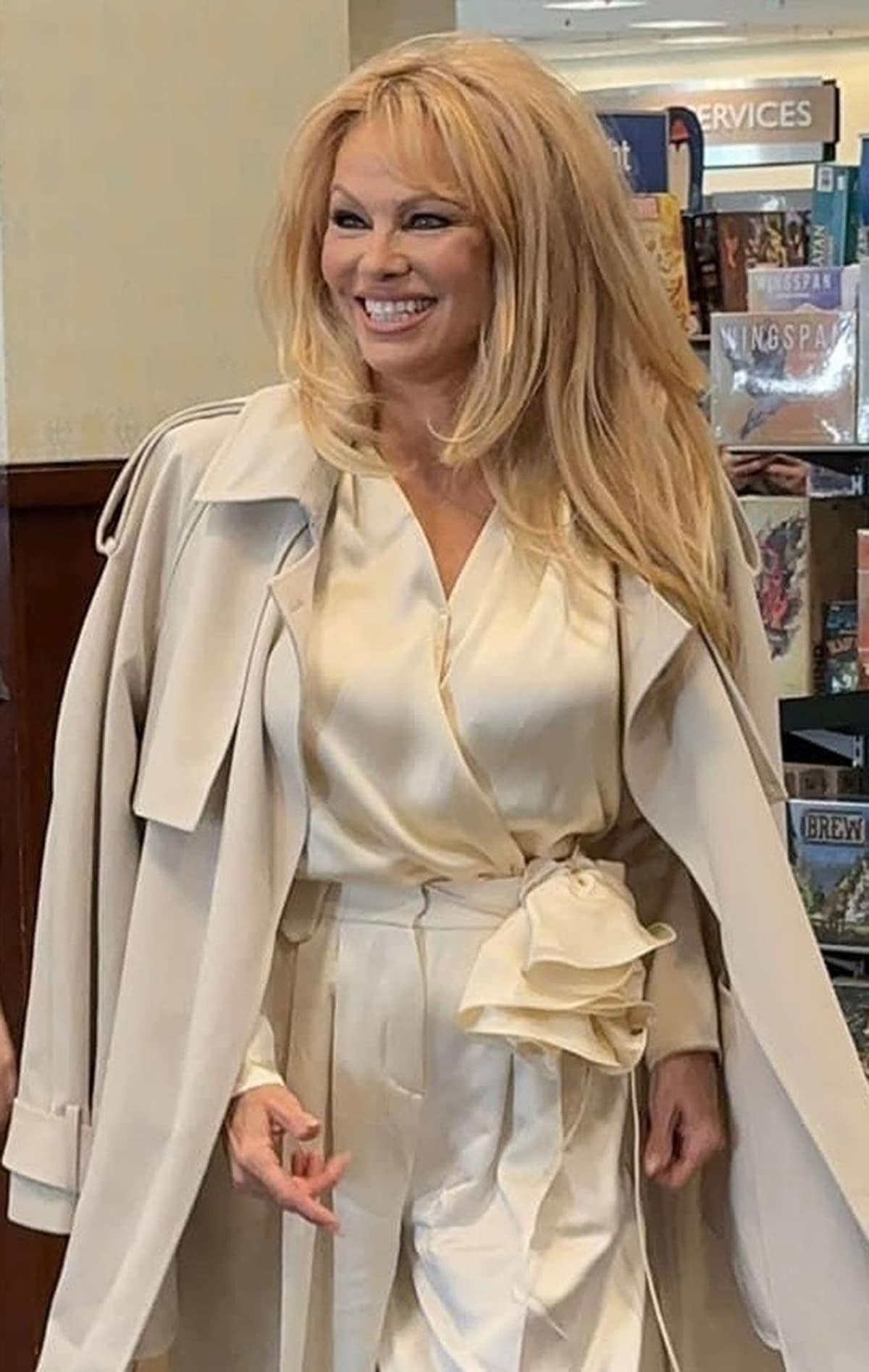 Pamela Anderson wearing a loose-fitting white jumpsuit with a matching coat at the Love, Pamela book signing on January 31, 2023