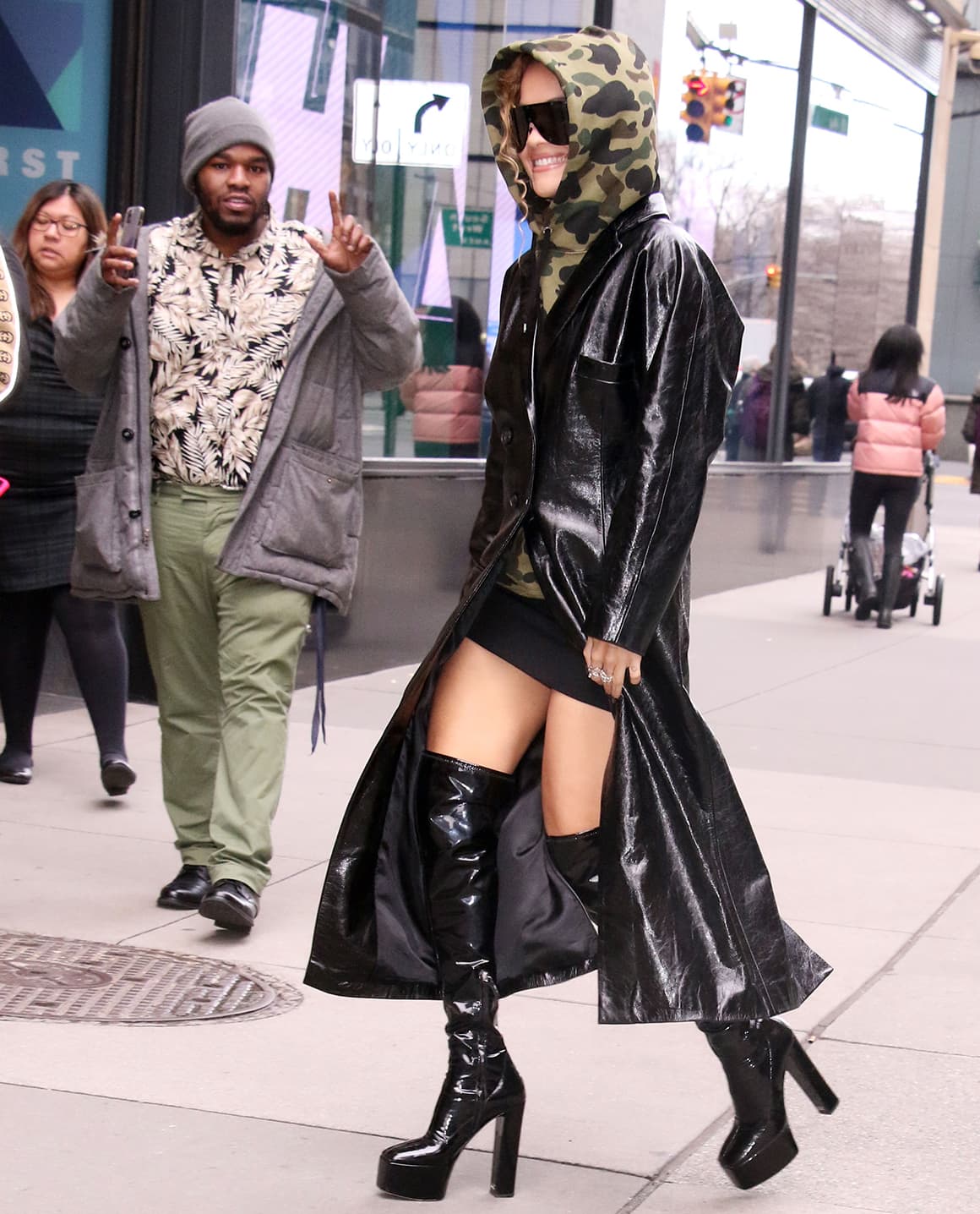 Rita Ora makes a racy statement in a mini skirt, thigh-high boots, and a leather trench coat with a camo hoodie