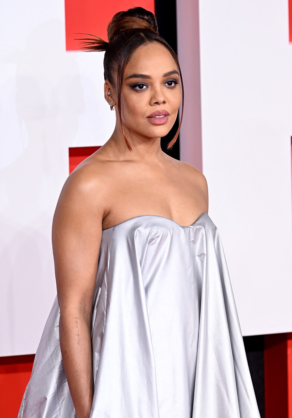 Tessa Thompson styles her tresses in a bun with face-framing fringe and wears black smokey eyeshadow with matte pink lip color