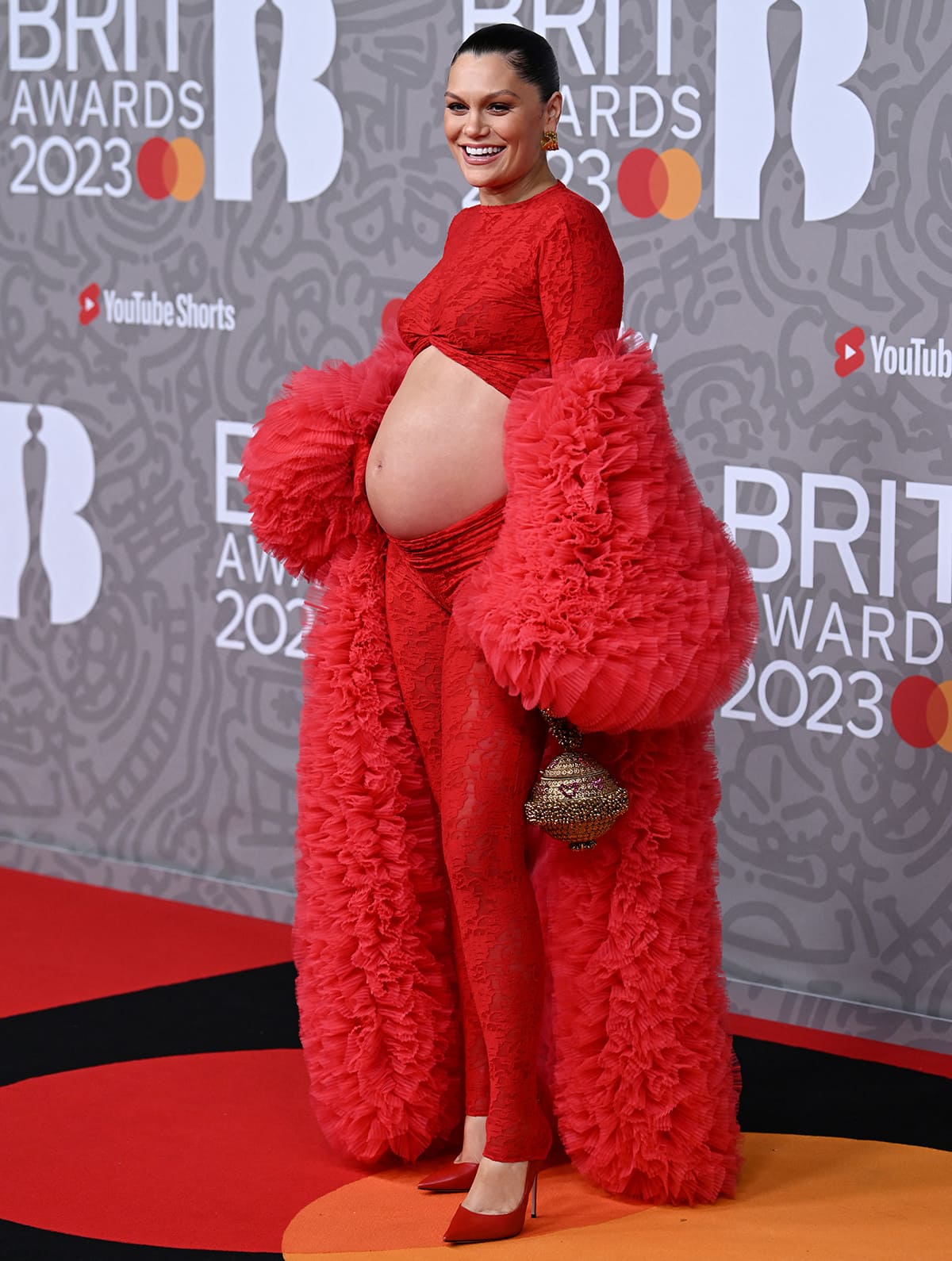 Jessie J adds drama to her modern maternity look with an oversized scarlet red coat with layers of ruffled tulle by Selezza
