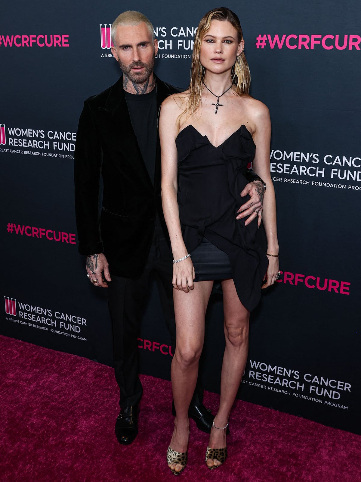 Adam Levine and Behati Prinsloo wear coordinating black outfits, with Levine in a velvet jacket and Prinsloo in an archival Vivienne Westwood mini dress