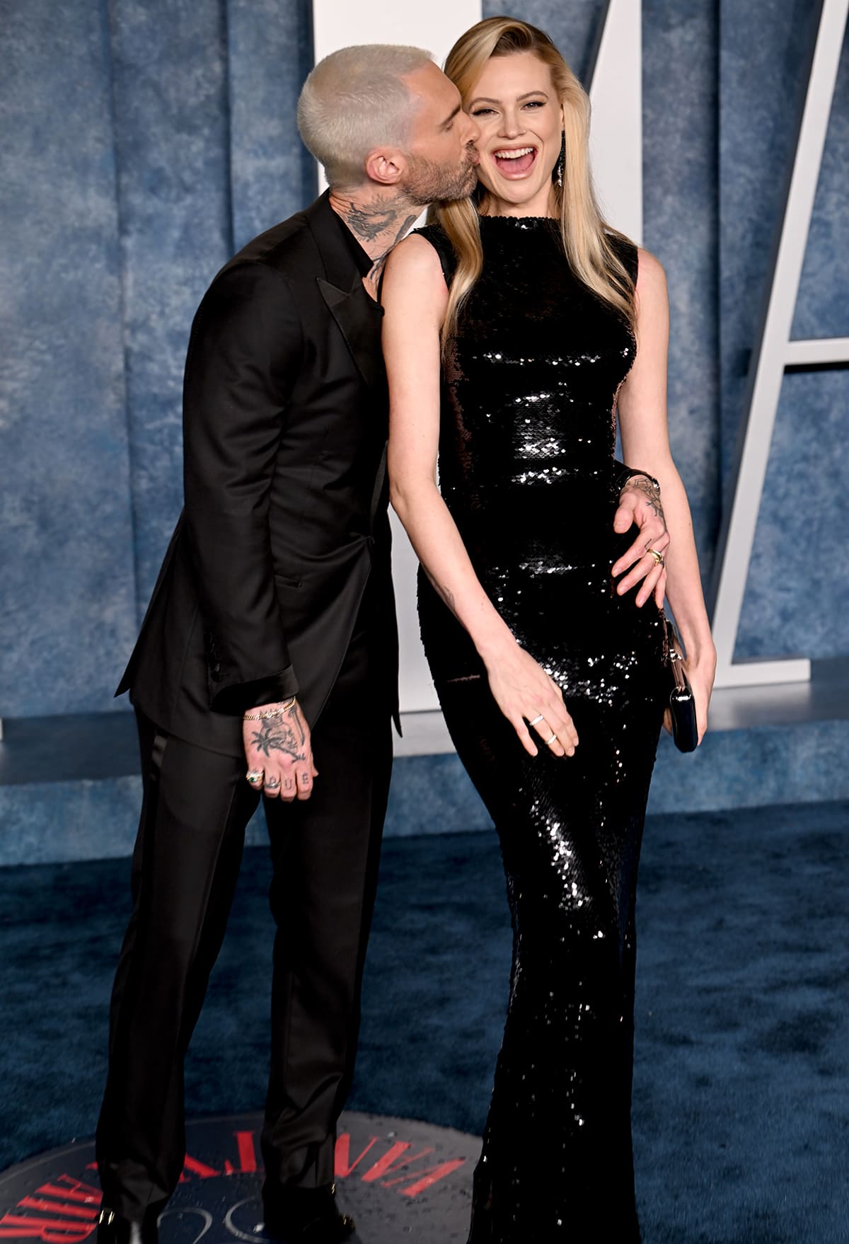 Adam Levine coordinates in a black tuxedo suit with a V-neck tee underneath and buckled shoes