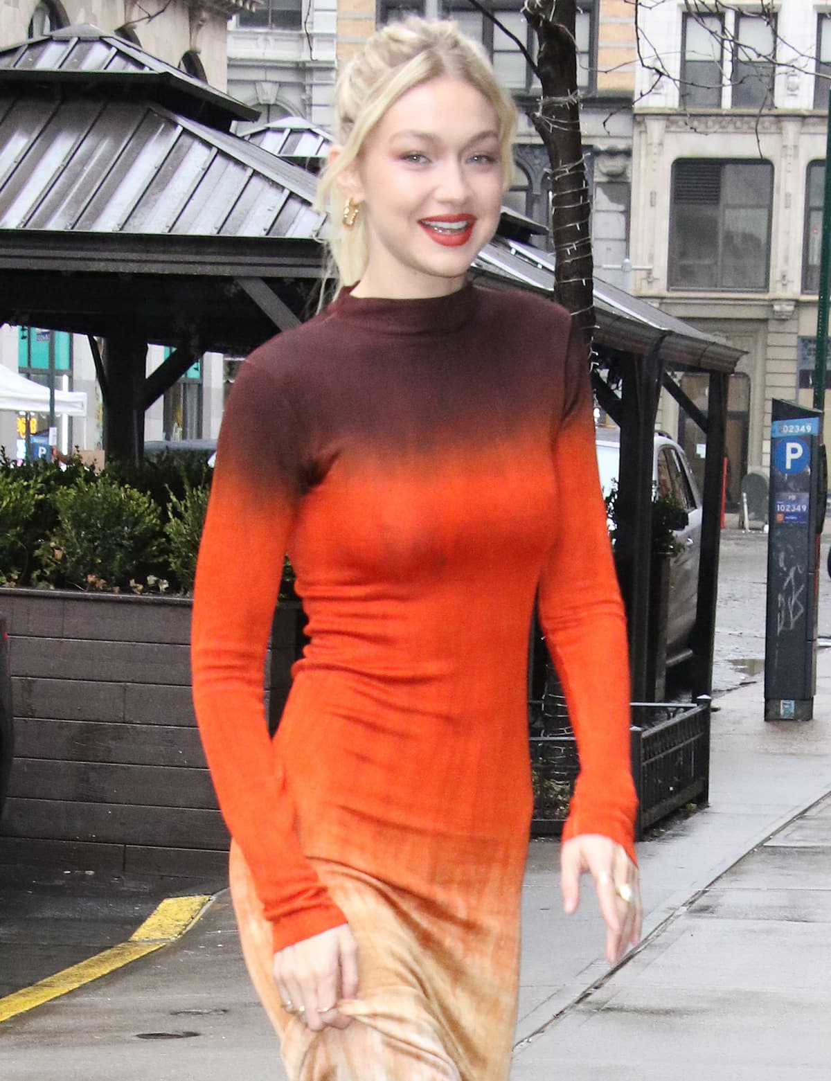 Gigi Hadid styles her blonde hair in a ponytail and wears bold red lip color to match her outfit