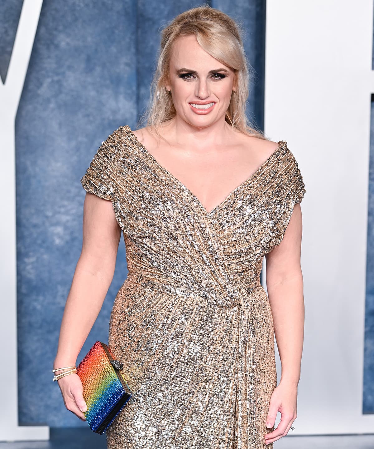 Rebel Wilson carries an LGBTQ-inspired rainbow clutch by Kurt Geiger and glams up with bronze smokey eyeshadow and pink lipstick