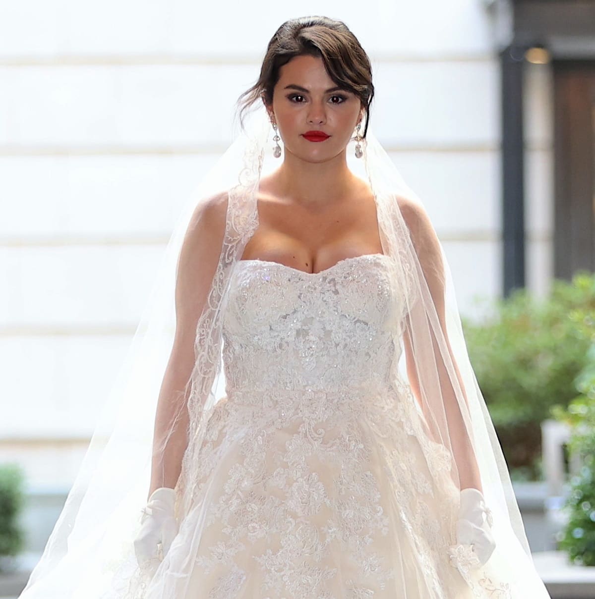 Selena Gomez sporting a strapless, lace-trimmed ballgown with a full skirt, long veil, and dangling baroque pearl earrings