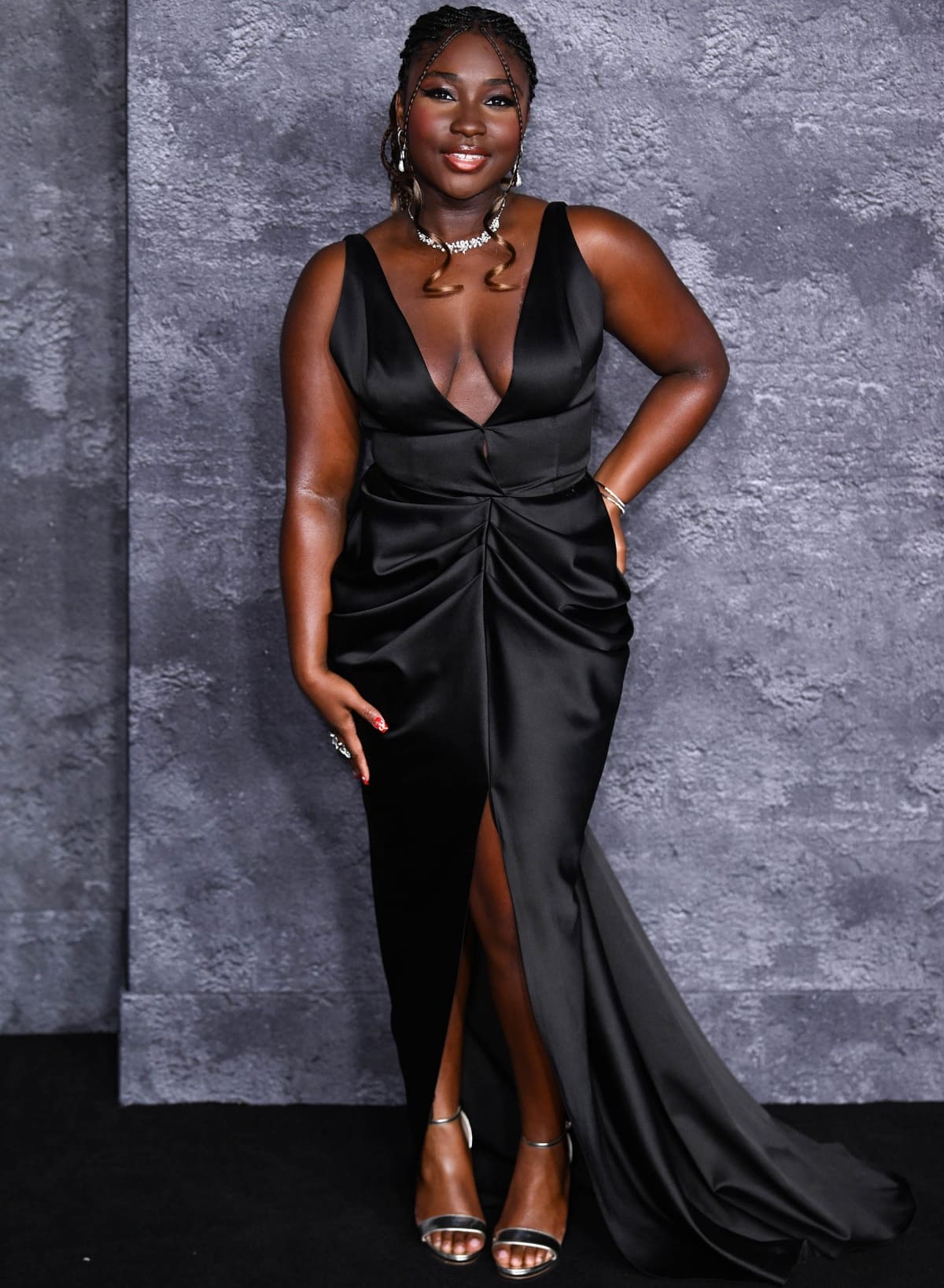 Lauryn Ajufo turned heads in a plunging black satin gown with ruched detailing and a thigh-high slit, finishing the look with shimmering silver ankle-strap heels at the Luther: The Fallen Sun premiere