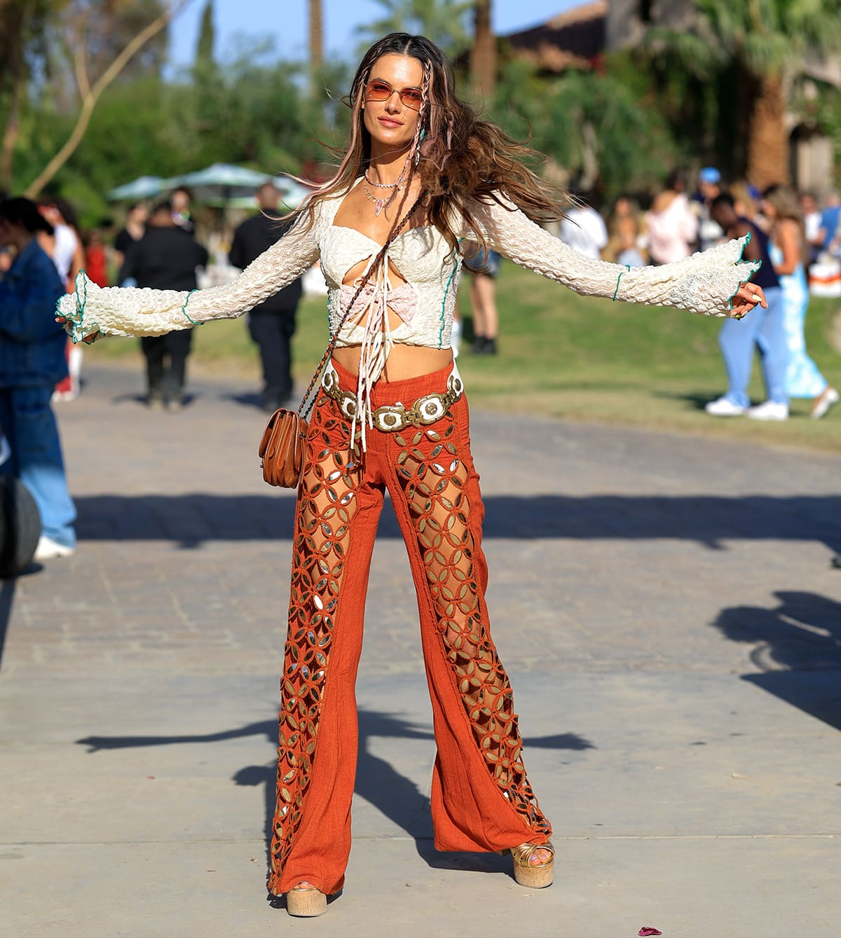 Alessandra Ambrosio showcases plenty of flesh in a hippie-inspired outfit composed of a Siedrés front-tie top and a pair of Raisa Vanessa burnt orange cutout pants