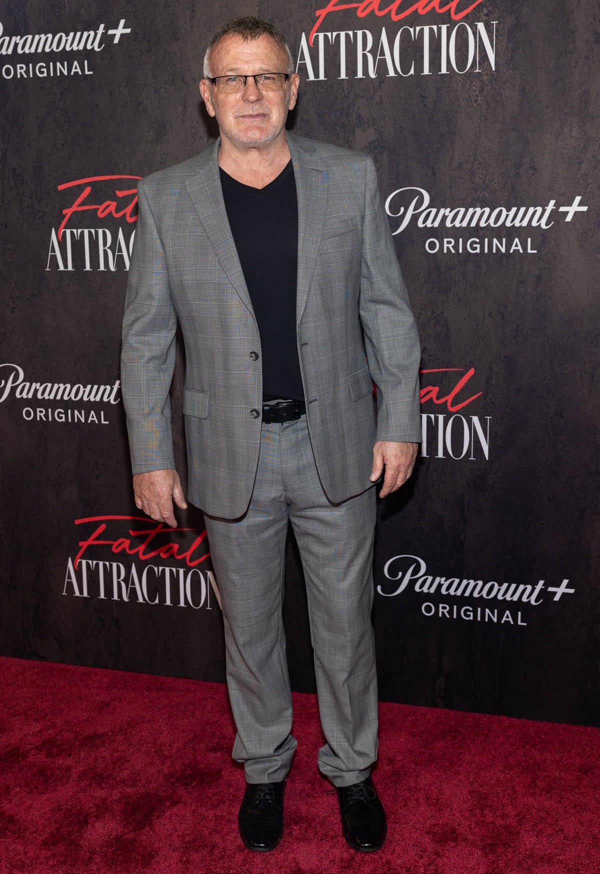 Brian Goodman exudes classic sophistication in a tailored gray plaid suit paired with a simple black shirt and polished black dress shoes at the Fatal Attraction premiere