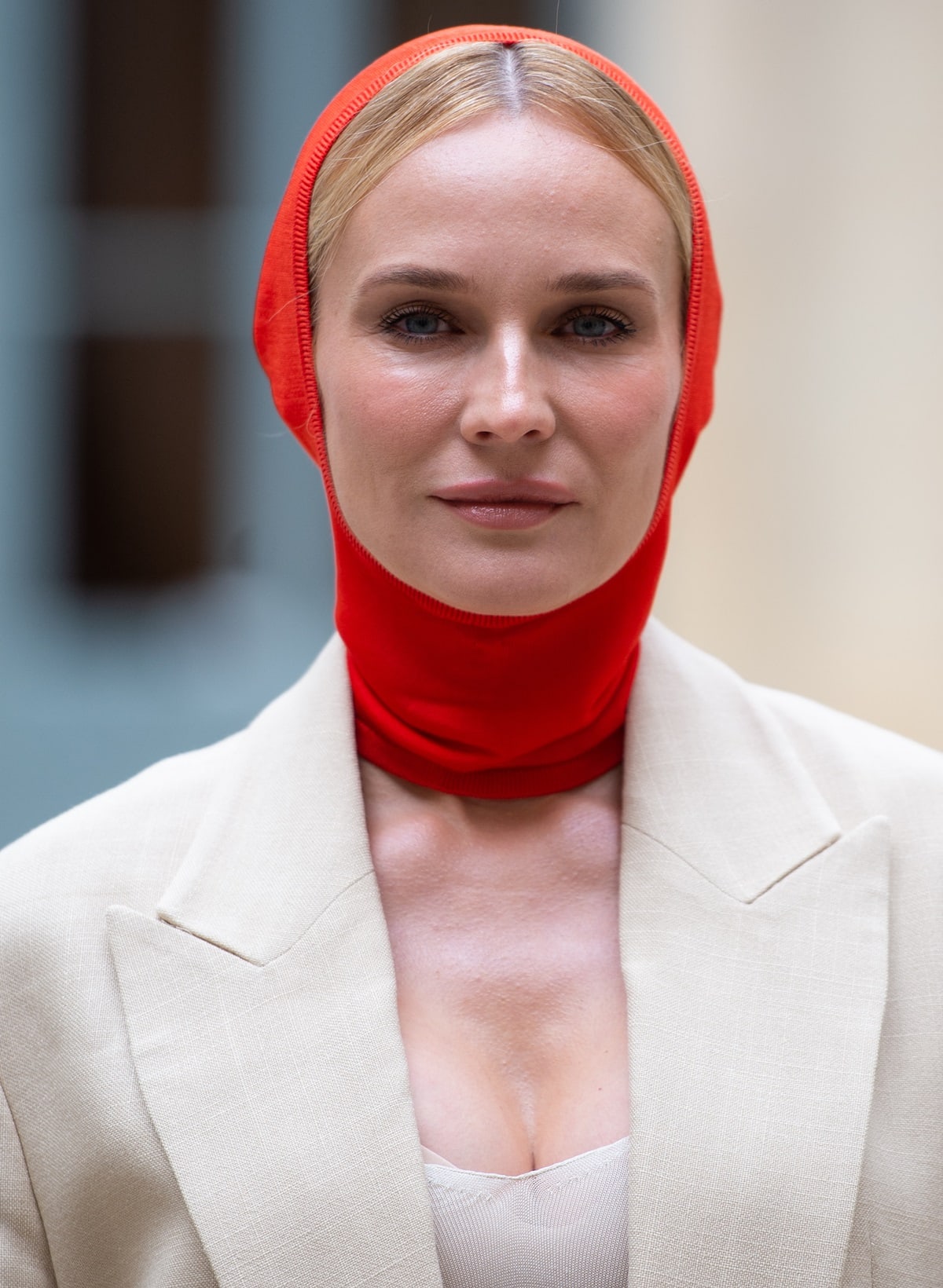 In a fashion-forward statement, Diane Kruger boldly dons a neon red balaclava paired with an oversized long beige blazer jacket
