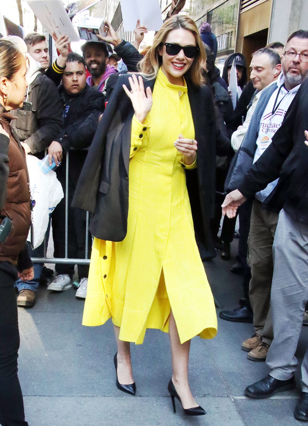 Elizabeth Olsen pairs her springtime yellow dress with black pumps and Ray-Ban Wayfarer sunglasses