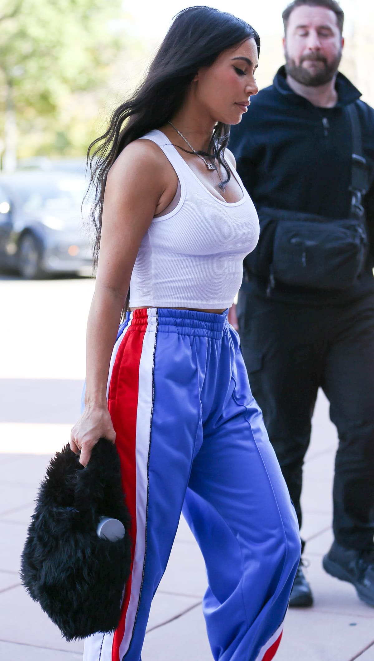 Kim Kardashian flaunted her midriff in a form-fitting white tank top paired with loose blue track pants with red and white stripes running down the sides