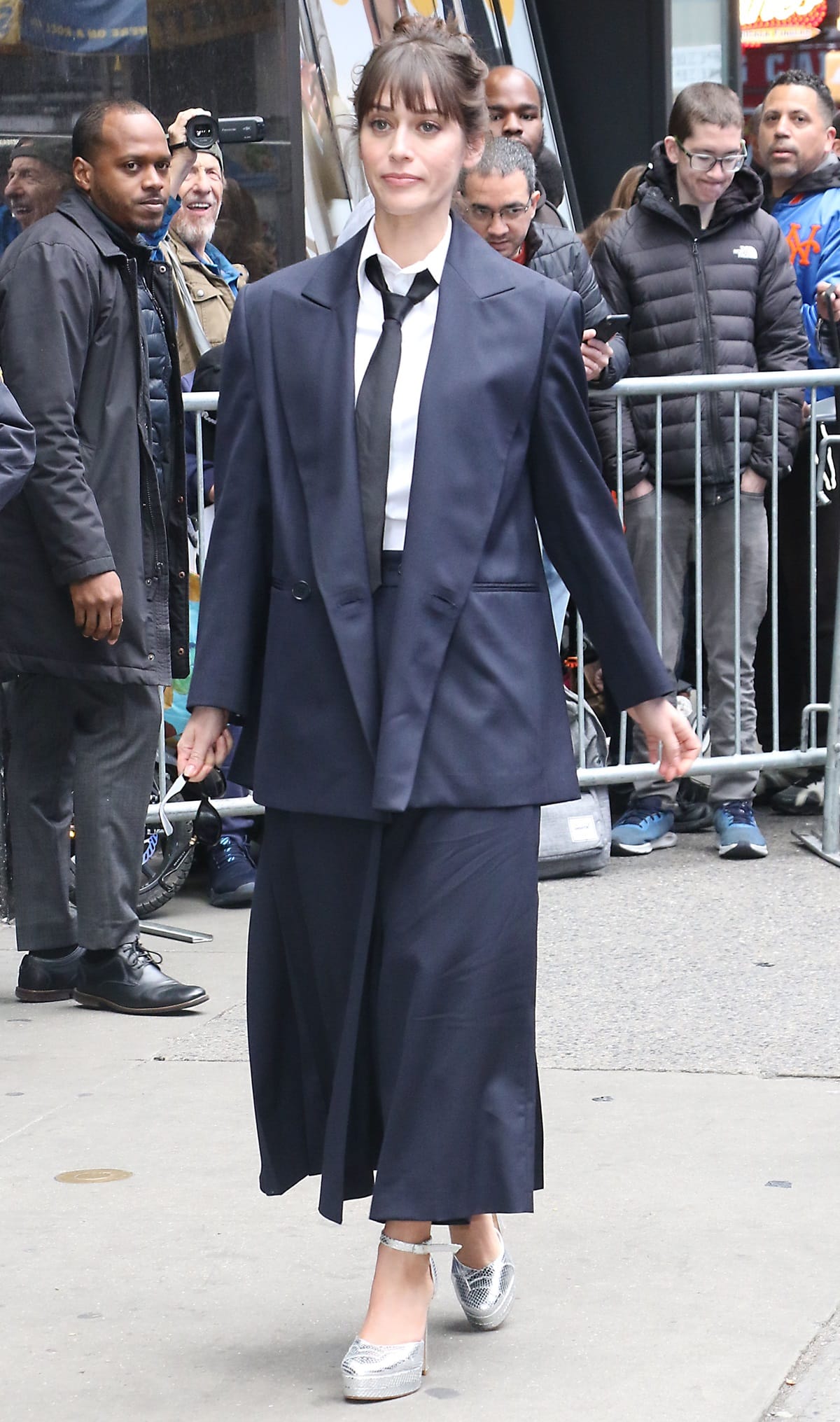 Lizzy Caplan steps out in an oversized navy suit, paired with a loose tie and silver platform heels, striking a balance between androgynous cool and feminine flair during her appearance in New York City