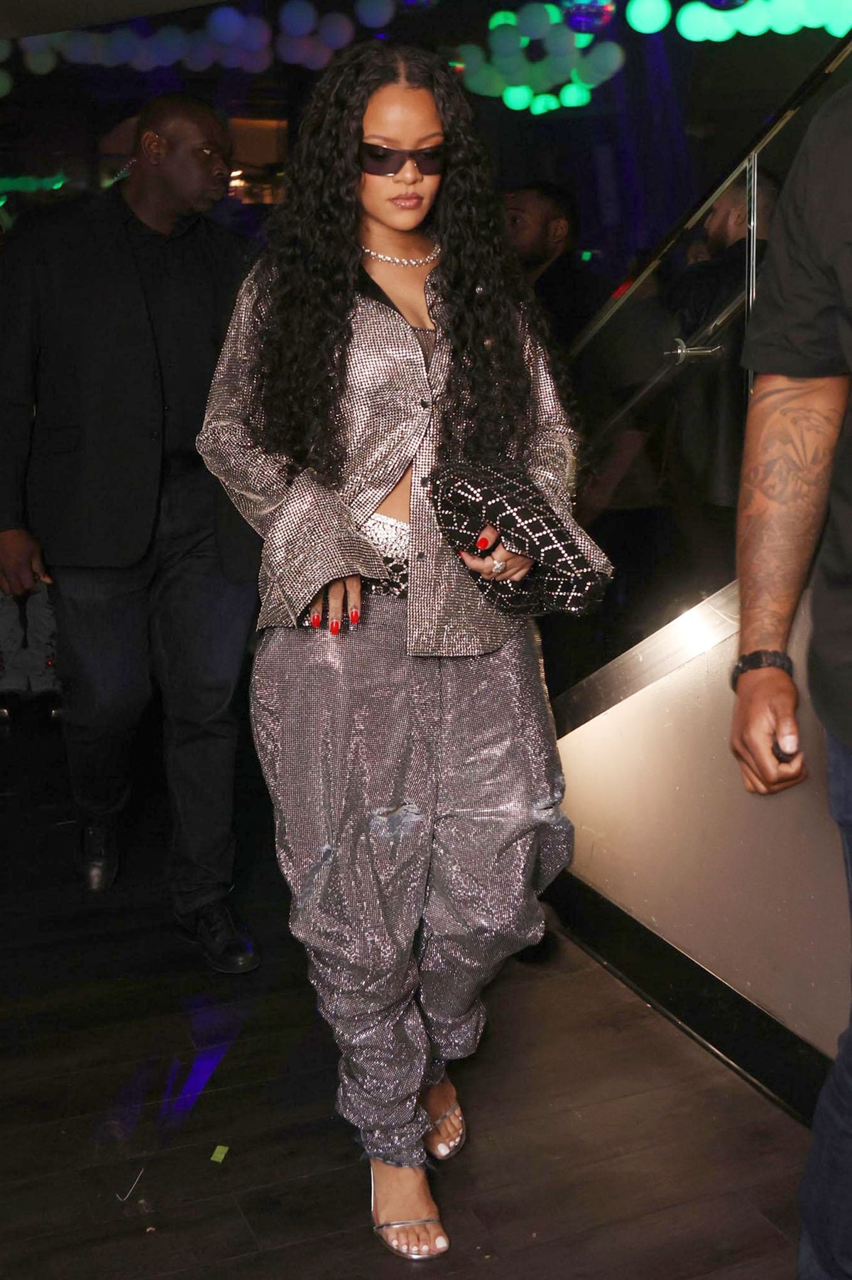 Rihanna stepped out of Miami's Story nightclub after her beau A$AP Rocky's performance looking radiant in a silver metallic silver Khaite top, matching JW Anderson pants, sunglasses, Reza diamond stud earrings, Amina Muaddi Giorgia metallic crystal-cuff sandals, and a Briony Raymond necklace