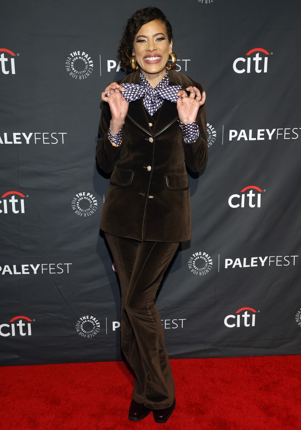 Tawny Cypress brings vintage charm to PaleyFest LA 2023 in a rich brown velvet suit paired with a bold patterned blouse and matching bow, exuding playful sophistication
