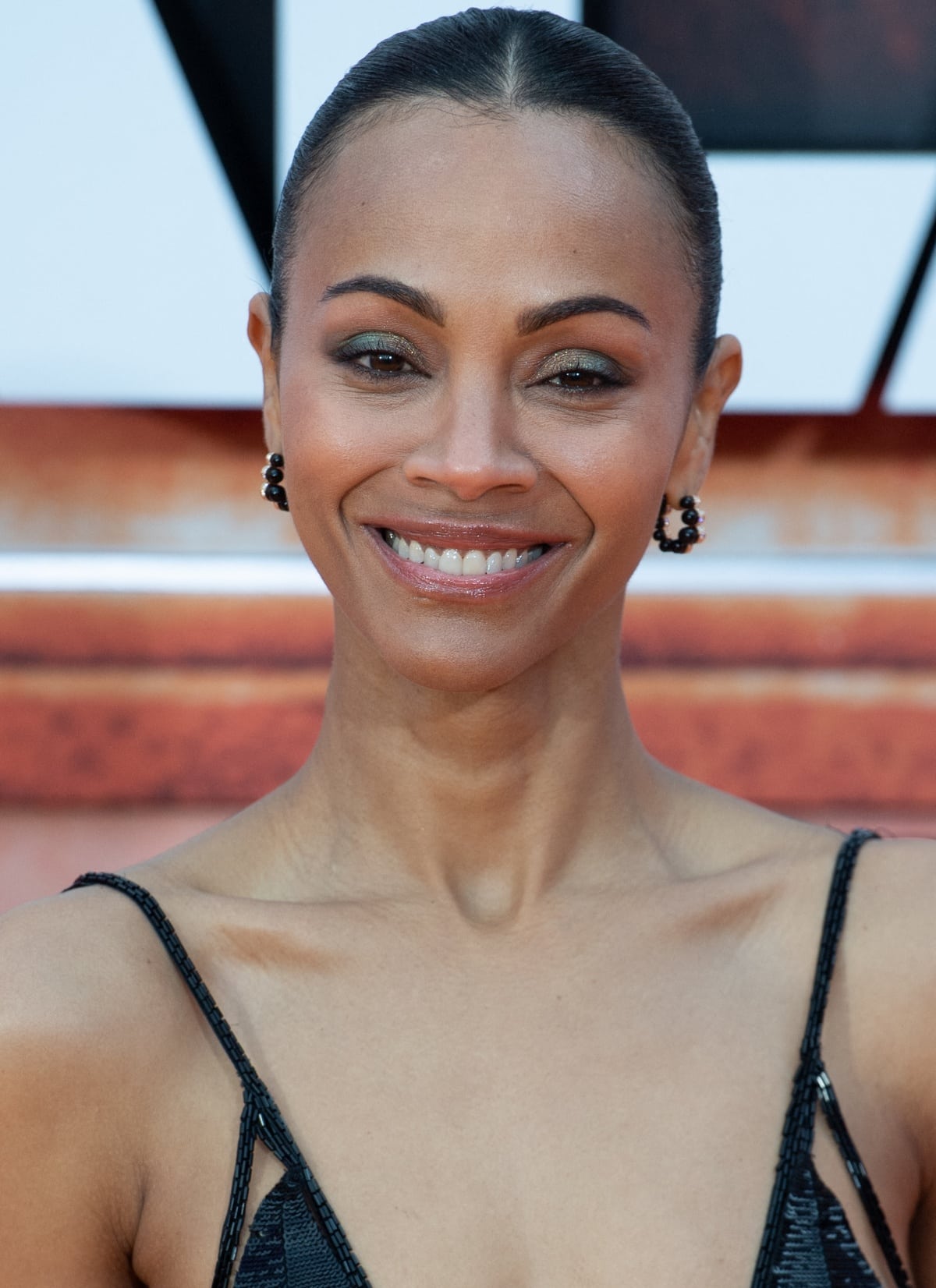 A slicked-back hairstyle, gray-and-green eye makeup, glossy nude lips, and Cartier earrings rounded out Zoe Saldana’s beauty look
