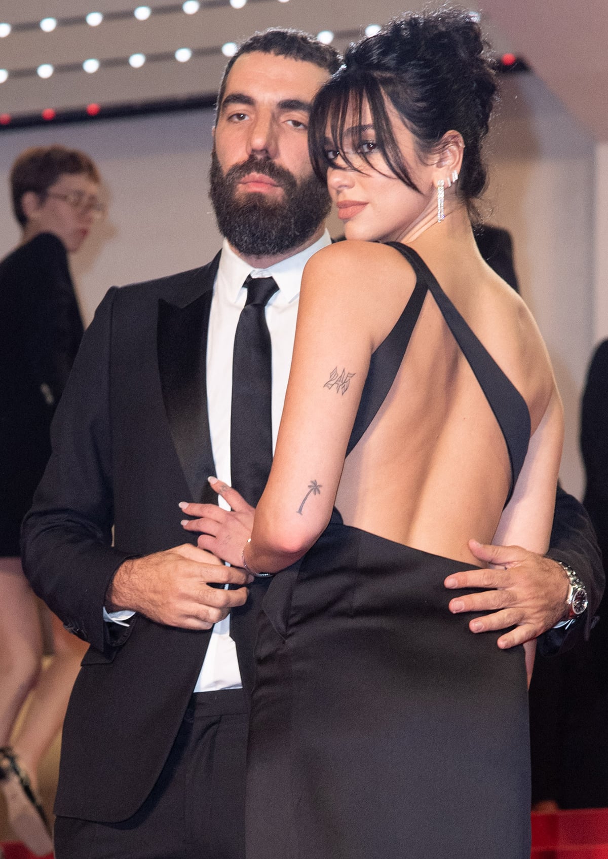 Dua Lipa showcases her sexy back and completes her glam with a fringed high bun, glittery smokey eye-makeup, and nude lipstick