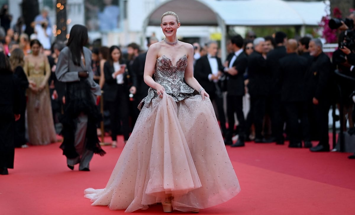 Elle Fanning lifts her Alexander McQueen gown to reveal towering nude platform heels, a practical yet elegant choice that added height, stability, and balance beneath the sweeping tulle train on the Cannes red carpet