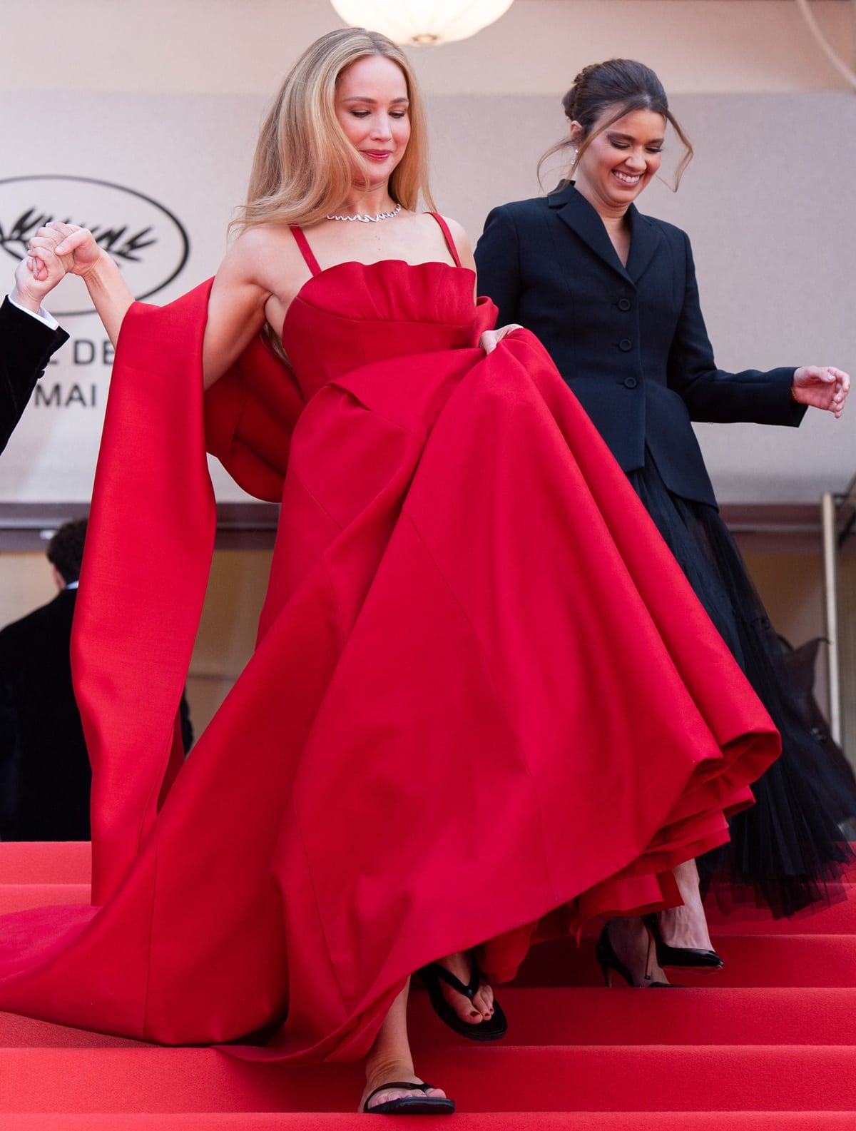 Arriving with Justine Ciarrocchi, Jennifer Lawrence made a striking fashion statement in a custom cardinal red Christian Dior Couture ball gown boasting a wrap-around shawl, a scalloped neckline, and a voluminous pleated skirt