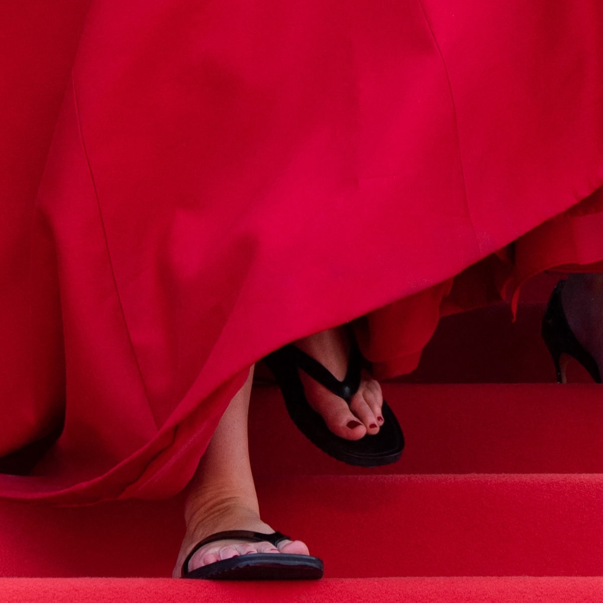 Lifting her hemline, Jennifer Lawrence revealed a pair of black flip-flop sandals underneath her red Christian Dior Couture ball gown