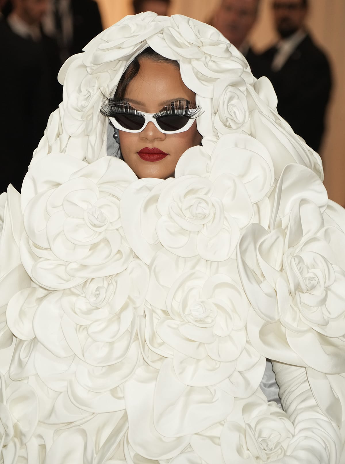 Rihanna adds a pop of bold red lip color to her all-white bridal look and wears a pair of sunglasses with false eyelashes adornment