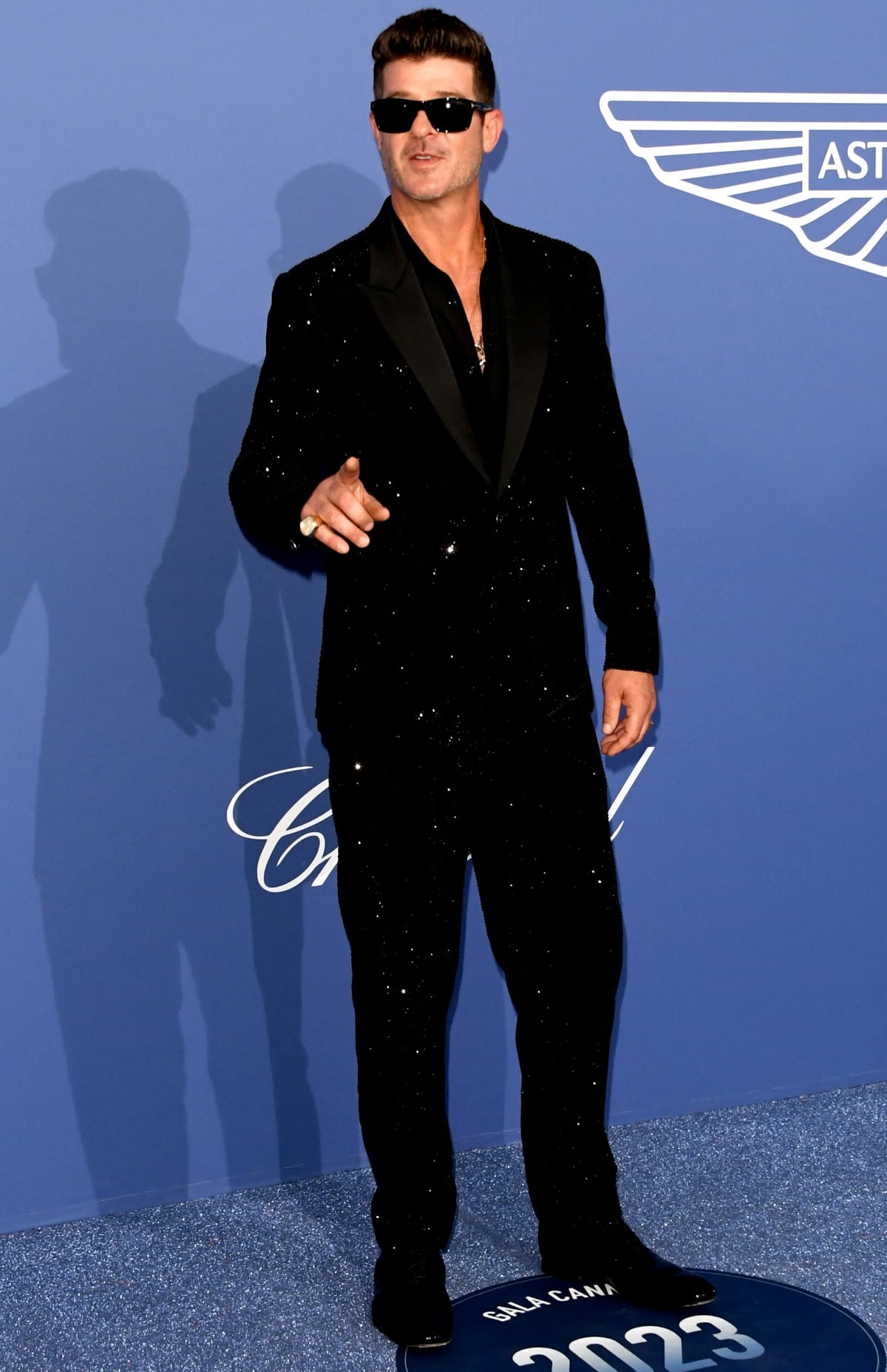 Robin Thicke wearing an all-black ensemble with sleek dress shoes and striking accessories