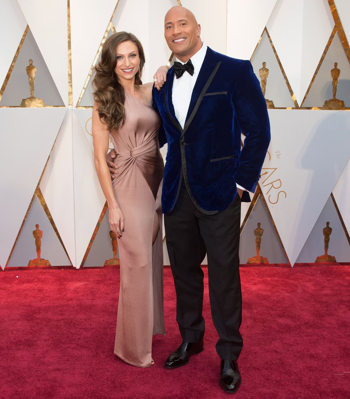 Dwayne Johnson and Lauren Hashian turned heads at the 89th Academy Awards on February 26, 2017, with Johnson in a custom deep blue velvet tuxedo and Hashian in a rose gold silk gown paired with matching studded ankle-strap heels that highlighted her legs