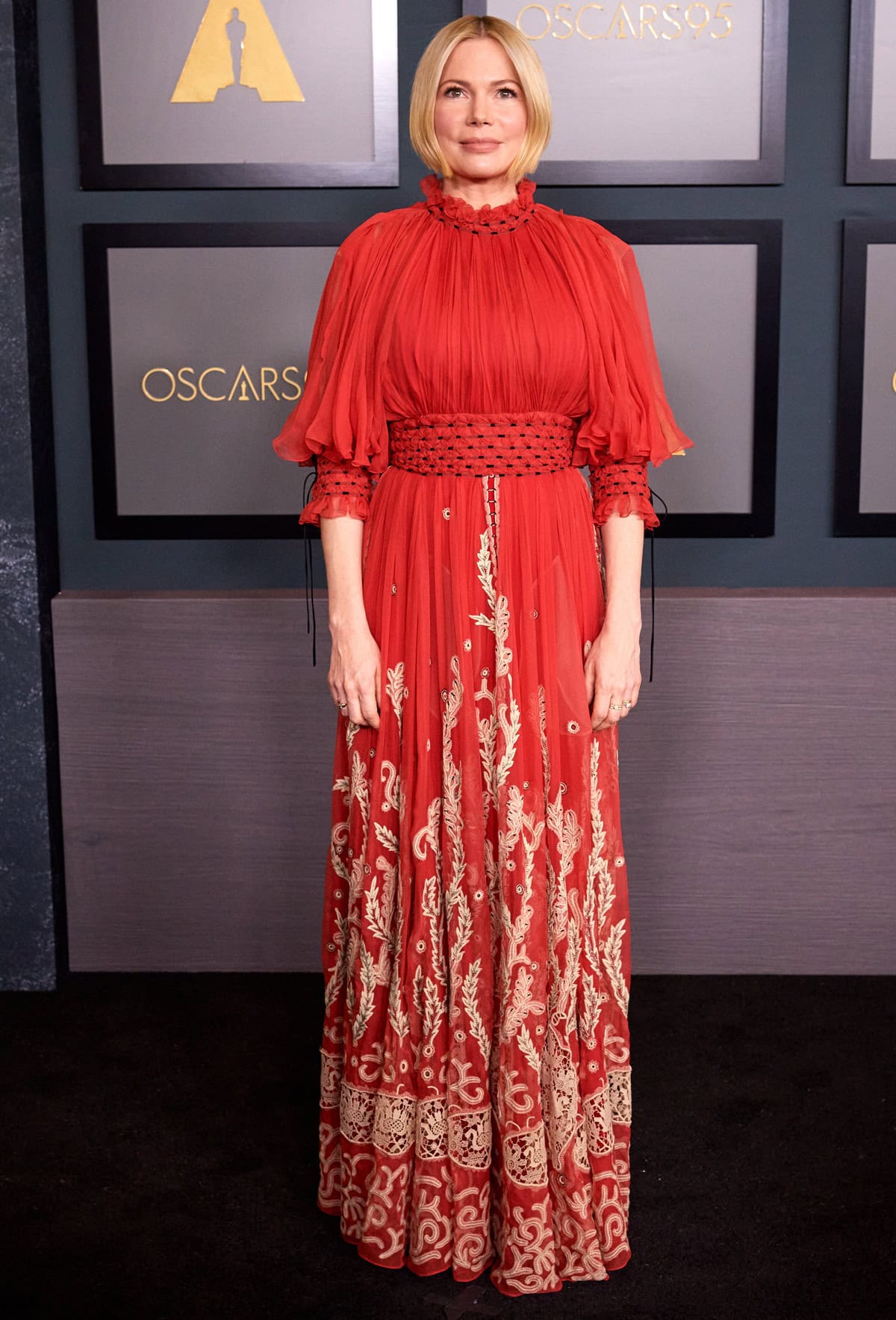 Michelle Williams embraced a regal, festive vibe in a red silk chiffon Dior Fall 2022 Haute Couture gown, intricately embroidered with botanical motifs and styled by Kate Young