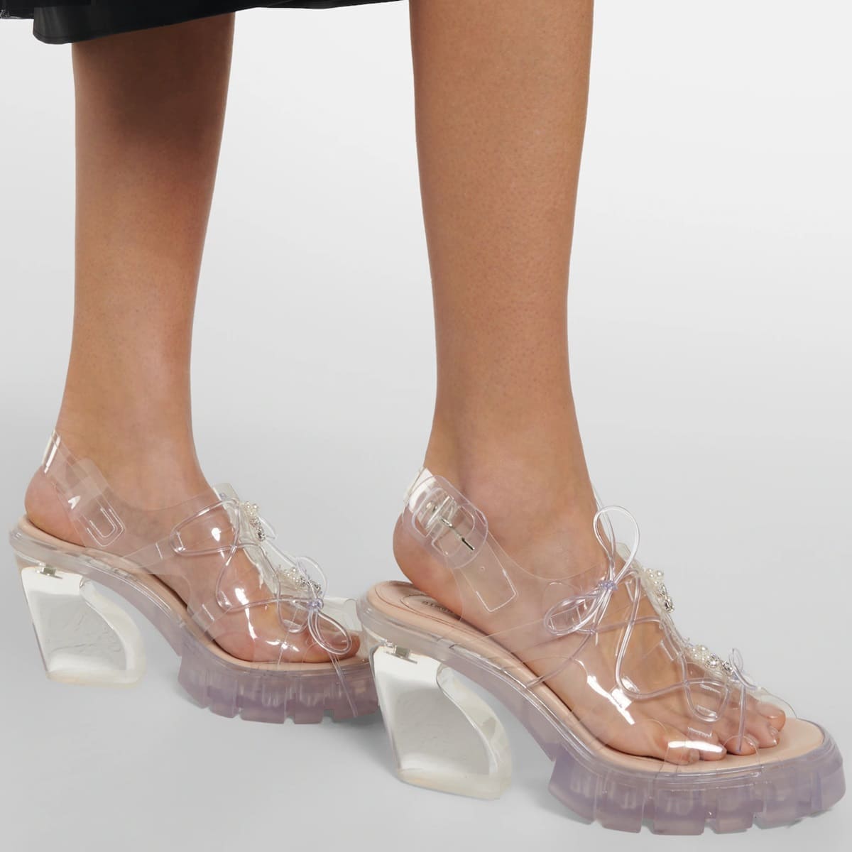 Simone Rocha's Trek sandals feature a lace-up design made of clear PVC, thick rubber soles, slanted block heels, and a comfortable leather insole
