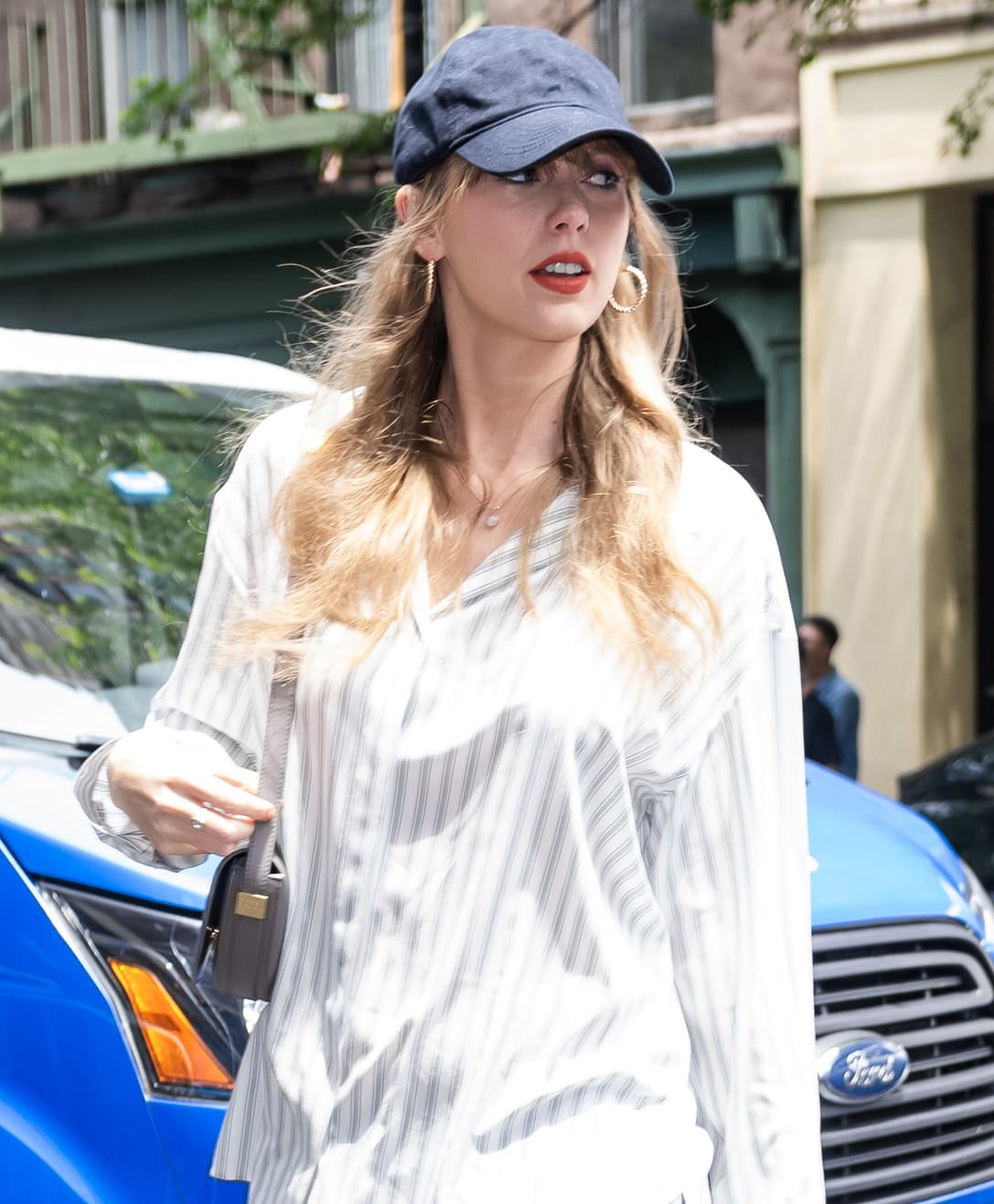 Taylor Swift tucks her wavy blonde tresses beneath a navy cap and wears bright red lipstick and blue eyeshadow