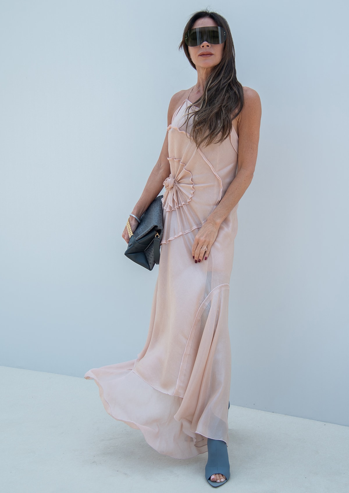 Victoria Beckham models her own design featuring a shimmering pale pink dress with a large rosette on the right hip and an asymmetrical hem