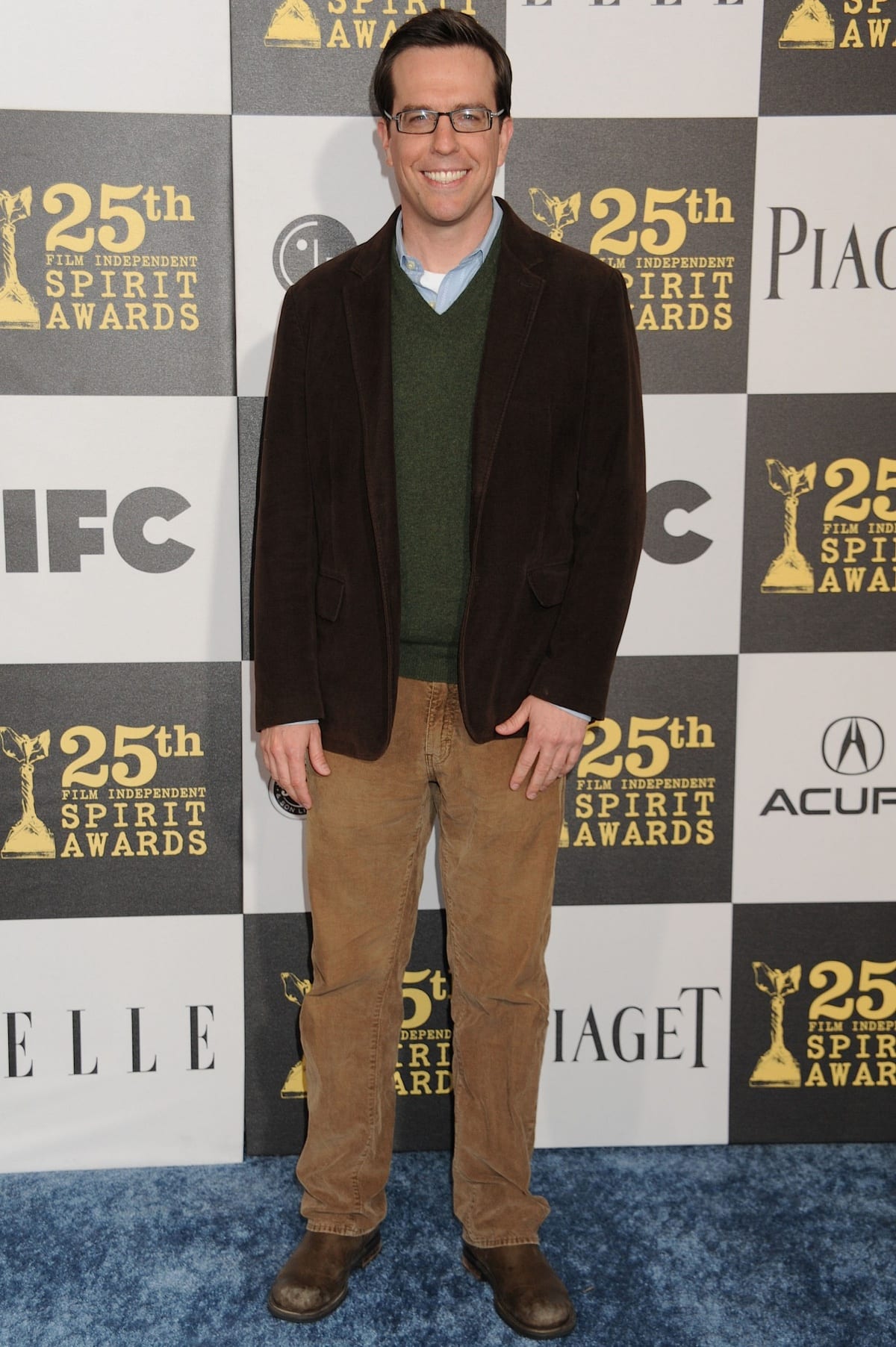 Ed Helms attending the 25th Film Independent Spirit Awards, dressed in a casual brown blazer, green sweater, and corduroy pants