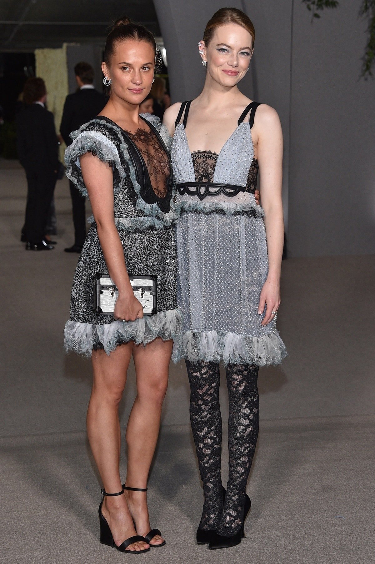 Alicia Vikander and Emma Stone stun in coordinating delicate lace dresses at a glamorous event, with Alicia pairing hers with strappy heels and Emma opting for lace-patterned tights
