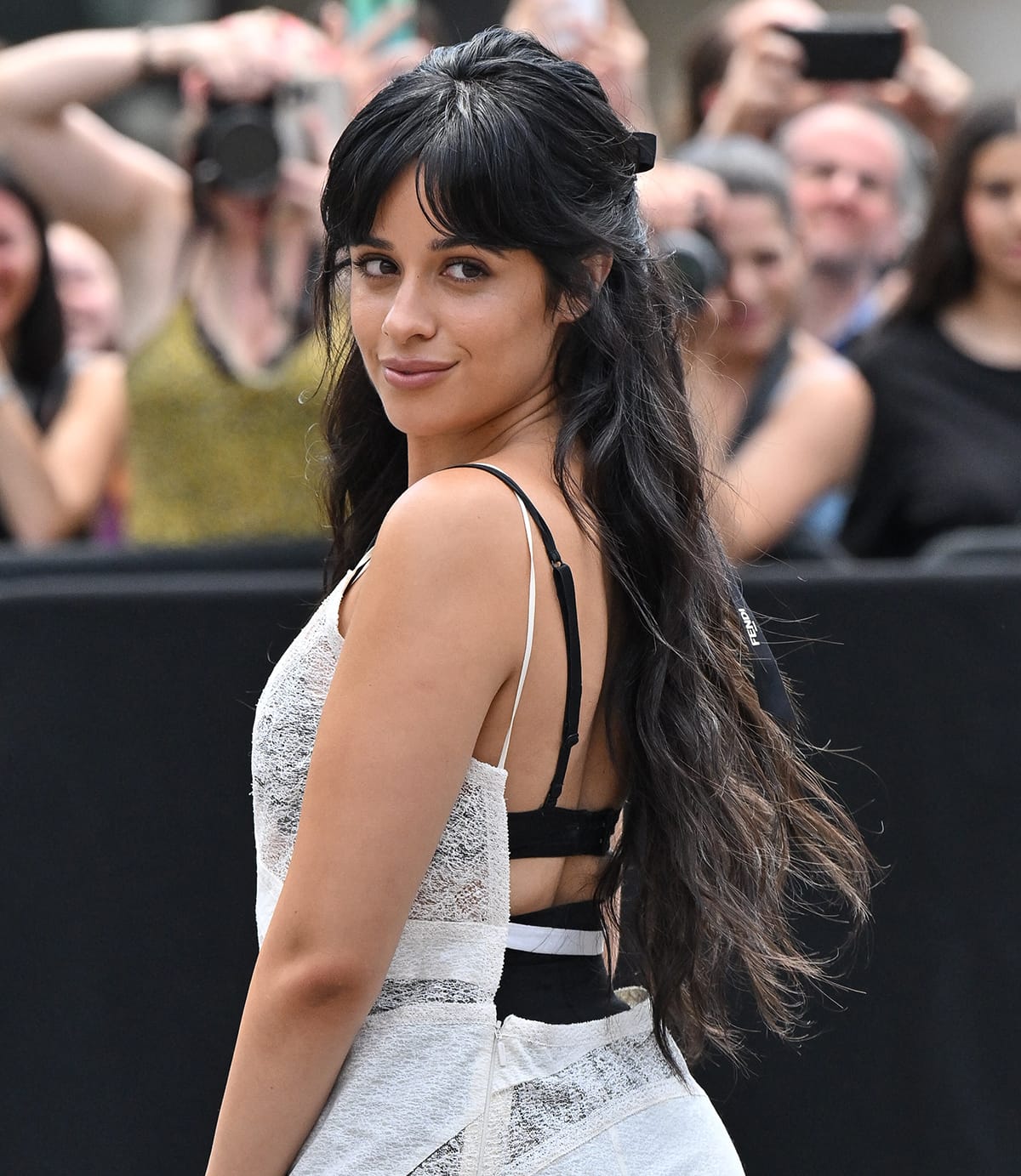 Camila Cabello wears a bronzed and nude makeup look and styles her raven tresses in loose waves before pulling them in a half-up, half-down style