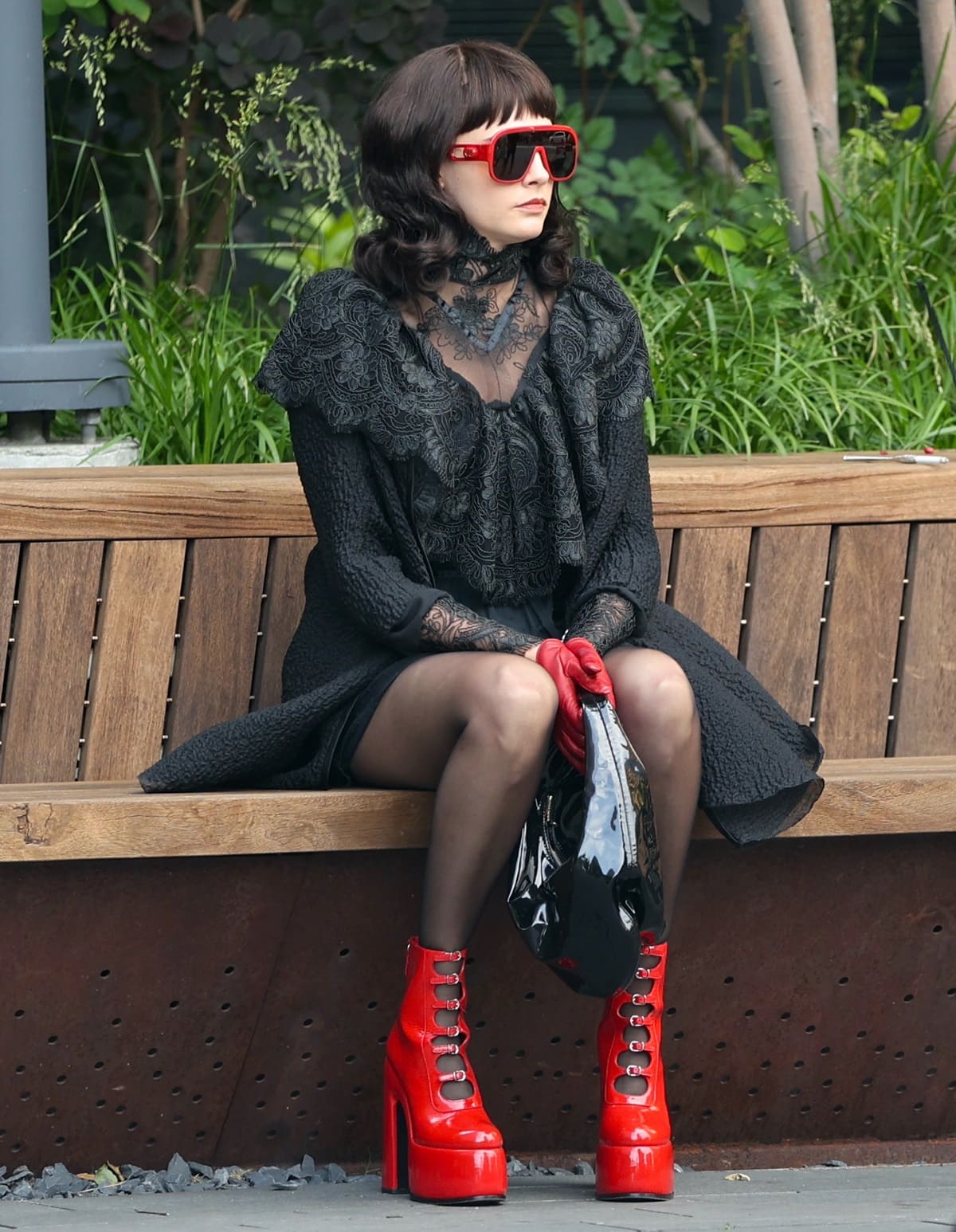 Cara Delevingne working on the set of American Horror Story's 12th season in New York City in a gothic black lace dress, a matching cloak, black stockings, and sky-high red patent leather heels