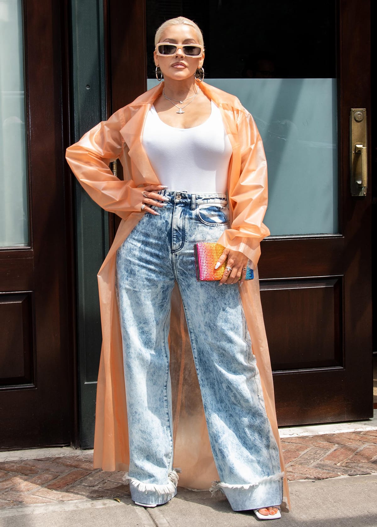 Christina Aguilera wears an orange raincoat with a white bodysuit and acid-washed jeans
