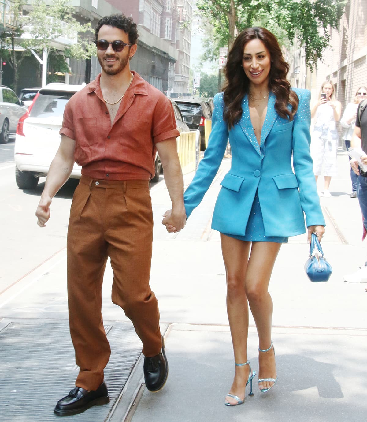 Kevin Jonas wears a terracotta shirt with brown pants, while his wife dons a blue Alex Perry skirt suit with crystal embellishments