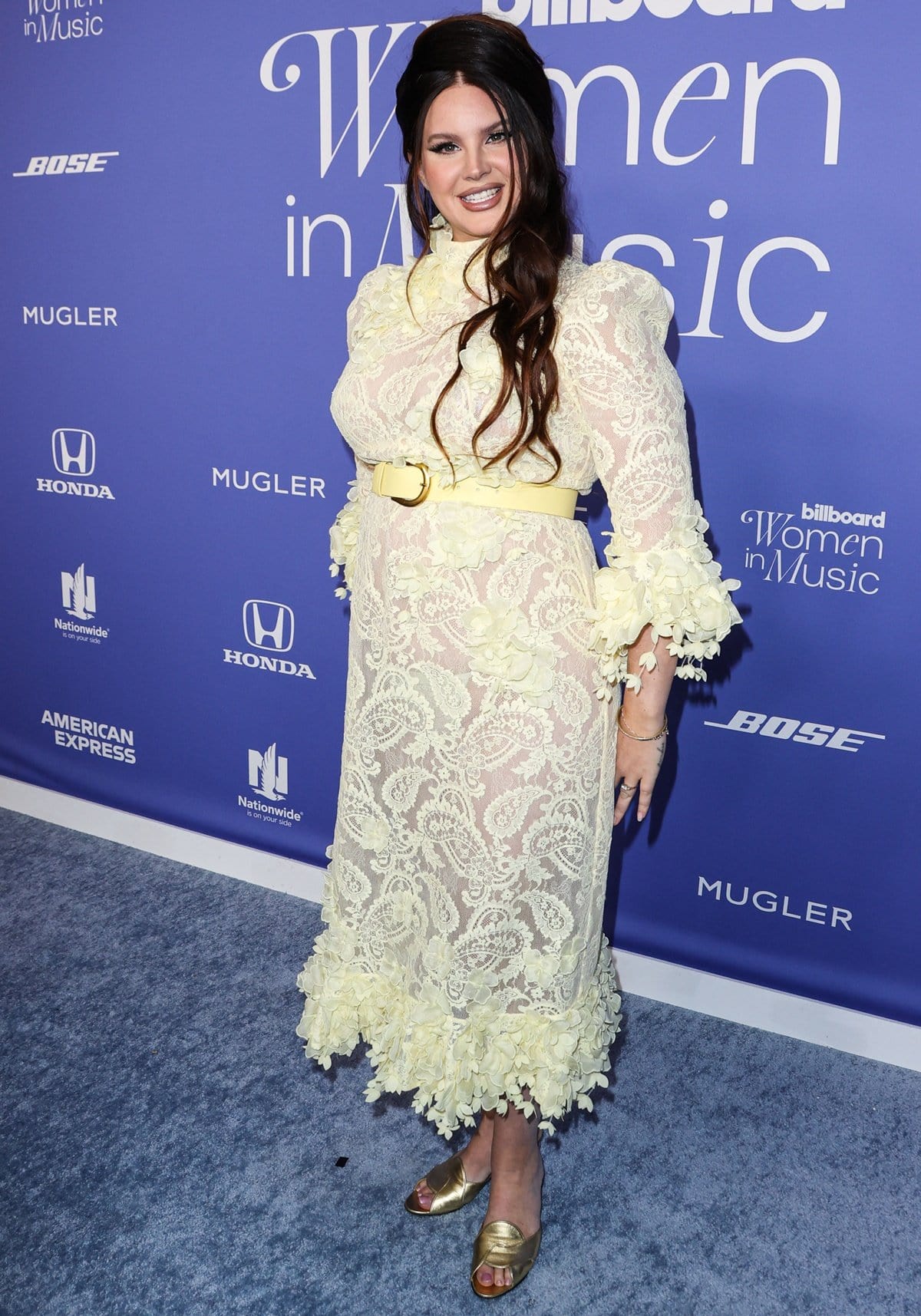 Lana Del Rey exudes vintage charm in a delicate yellow lace Zimmermann dress adorned with floral appliqués, paired with metallic gold peep-toe heels, at the 2023 Billboard Women in Music event