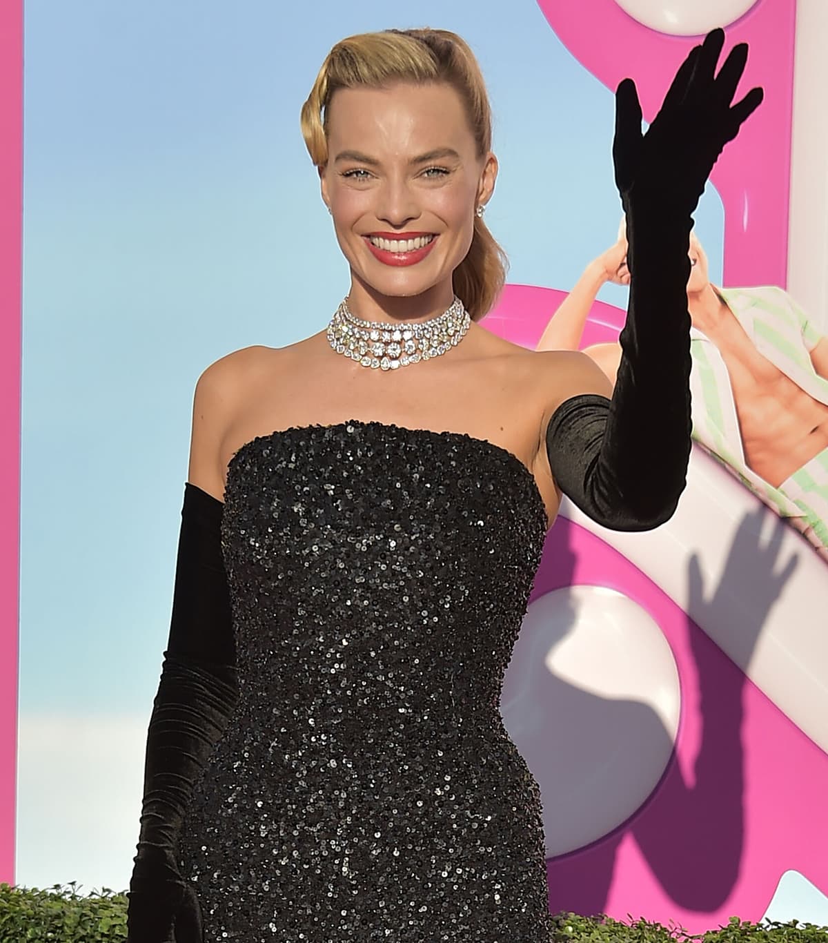 Margot Robbie completes her 1960s Barbie look with opera gloves, diamond jewelry, a retro ponytail, and a bright red lip color