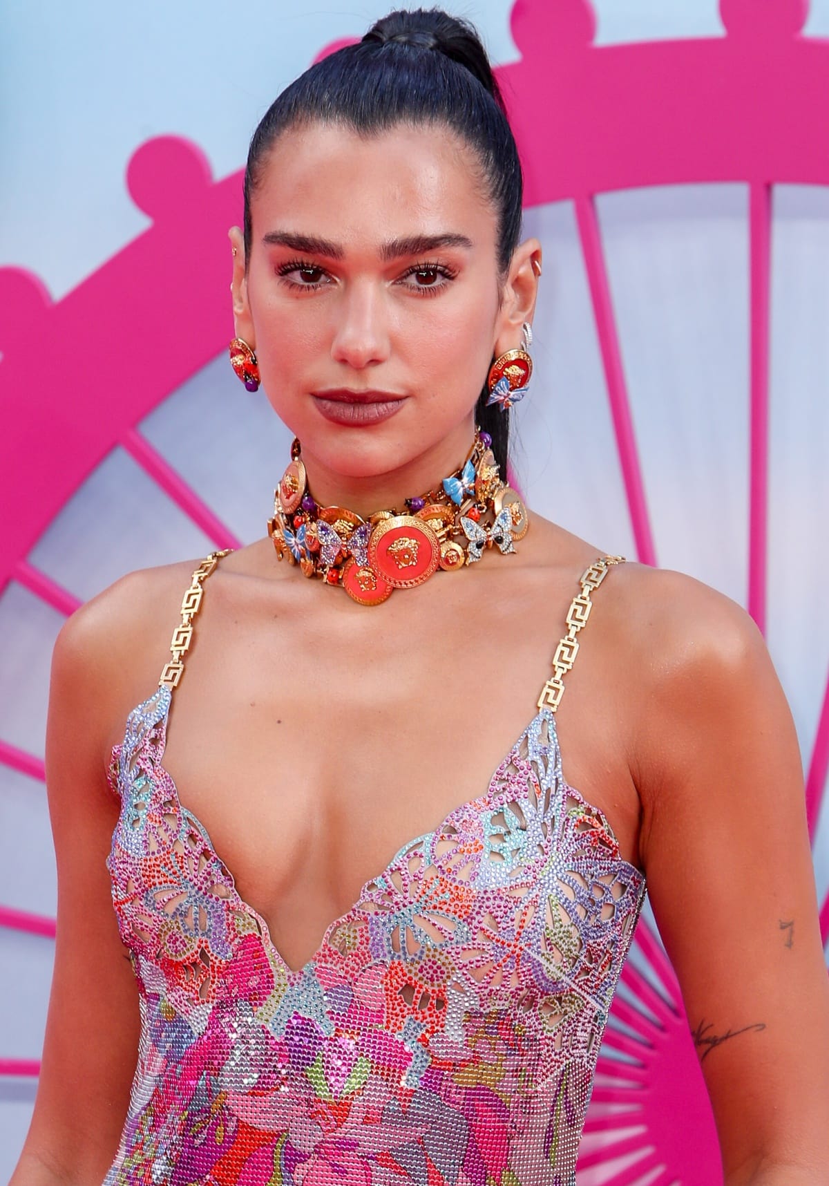 Dua Lipa showcasing her sheer multicolored dress from her “La Vacanza” collection with Versace decorated with a chunky choker and several other enchanting accessories