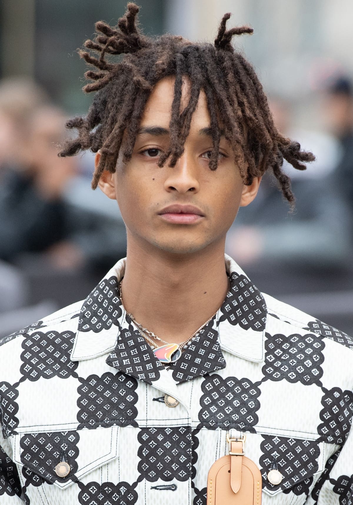 Jaden Smith attends a fashion event, showcasing his unique style with a geometric patterned jacket and distinctive hairstyle