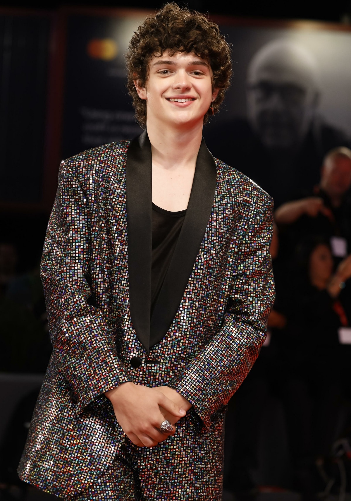 Noah Jupe dazzles on the red carpet, wearing a shimmering, multi-colored suit with a sleek black lapel, showcasing his bold fashion sense
