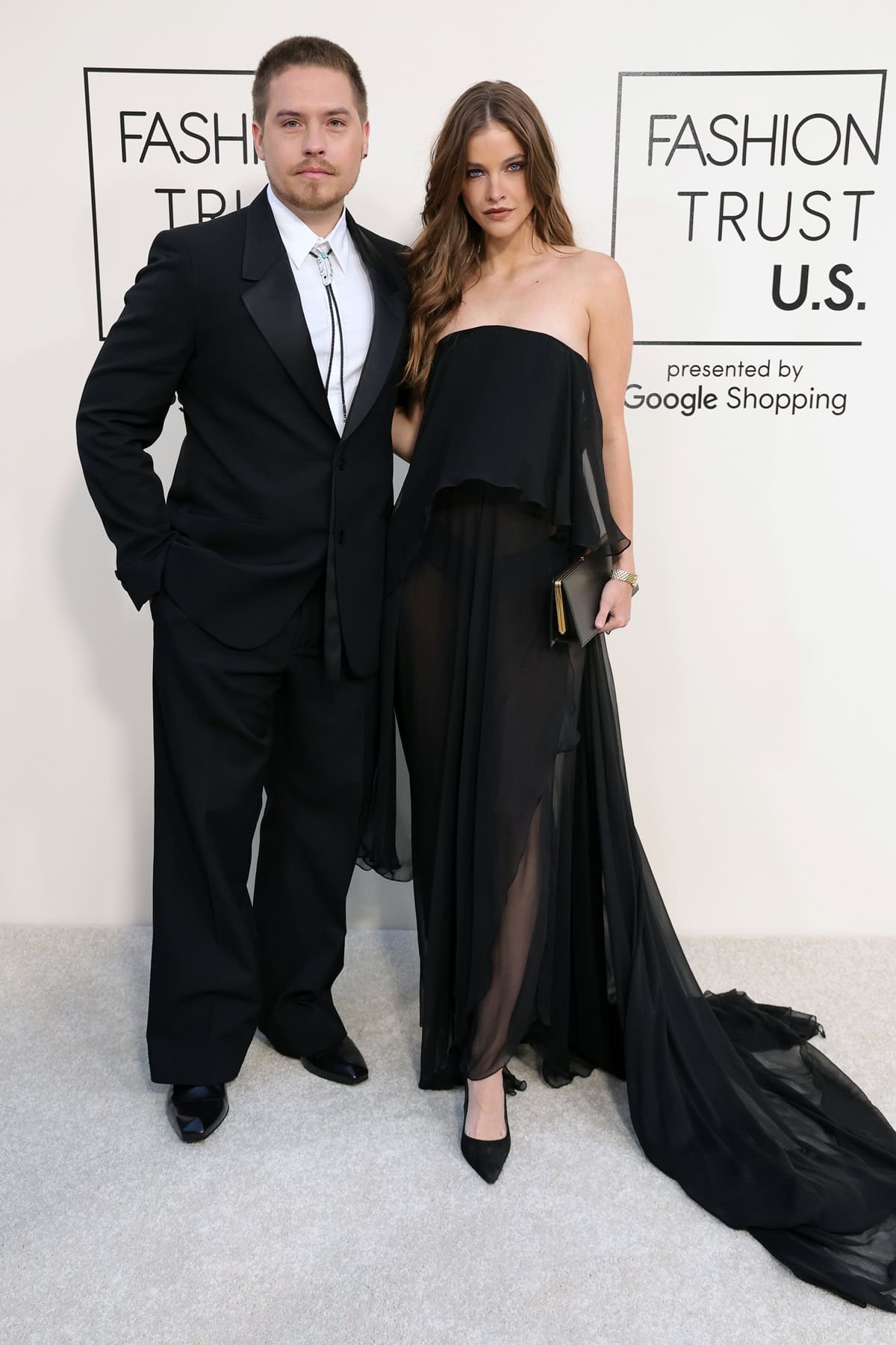 Barbara Palvin stunned in a strapless black Roberto Cavalli gown with an asymmetrical ruffled skirt, pairing the flowing look with pointed-toe black heels that helped balance her height next to Dylan’s polished black suit, square-toe shoes, and bolo tie