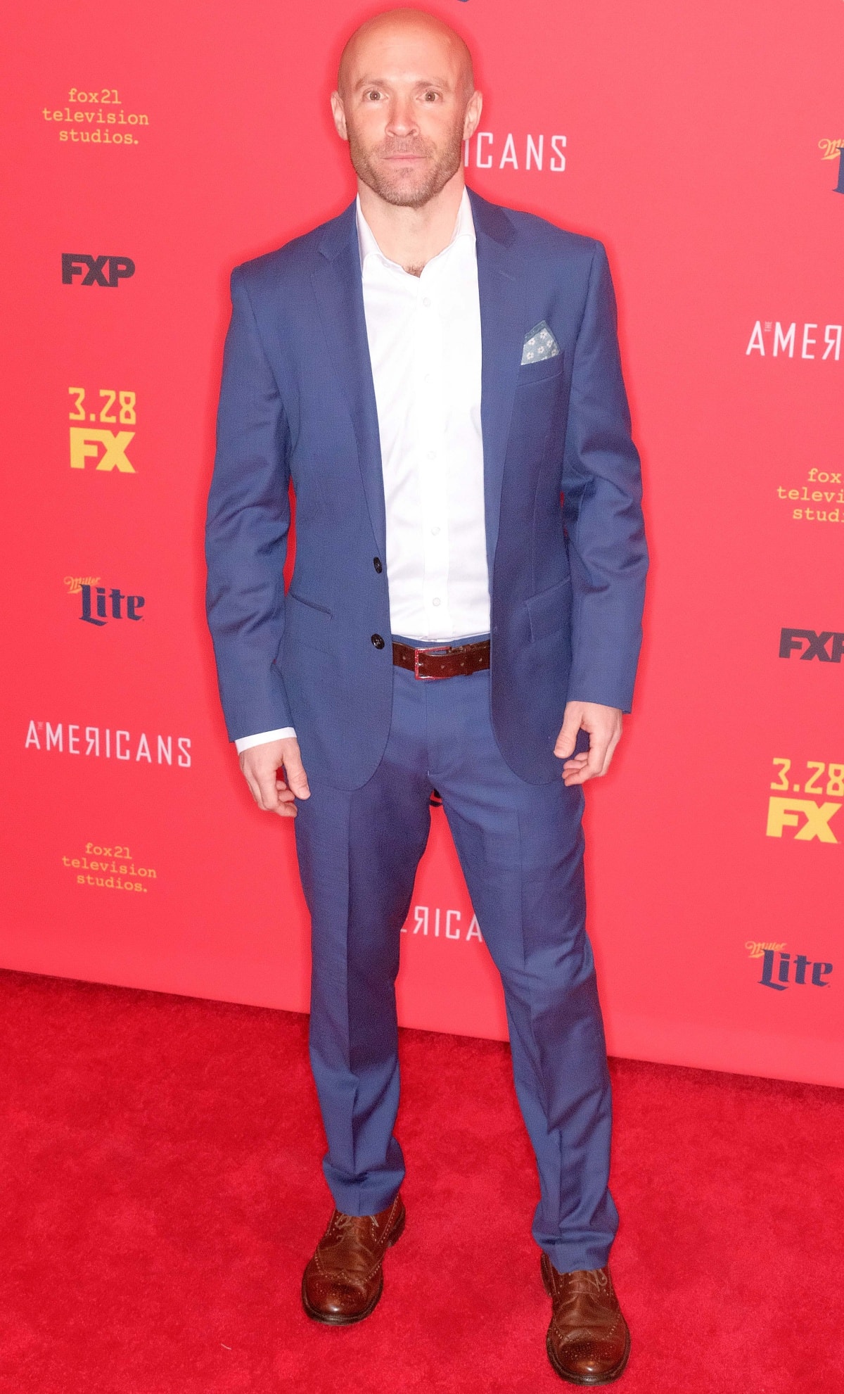 Aaron Roman Weiner kept it classic in a blue suit with a patterned pocket square, grounding the look with polished brown brogue dress shoes at the premiere of The Americans